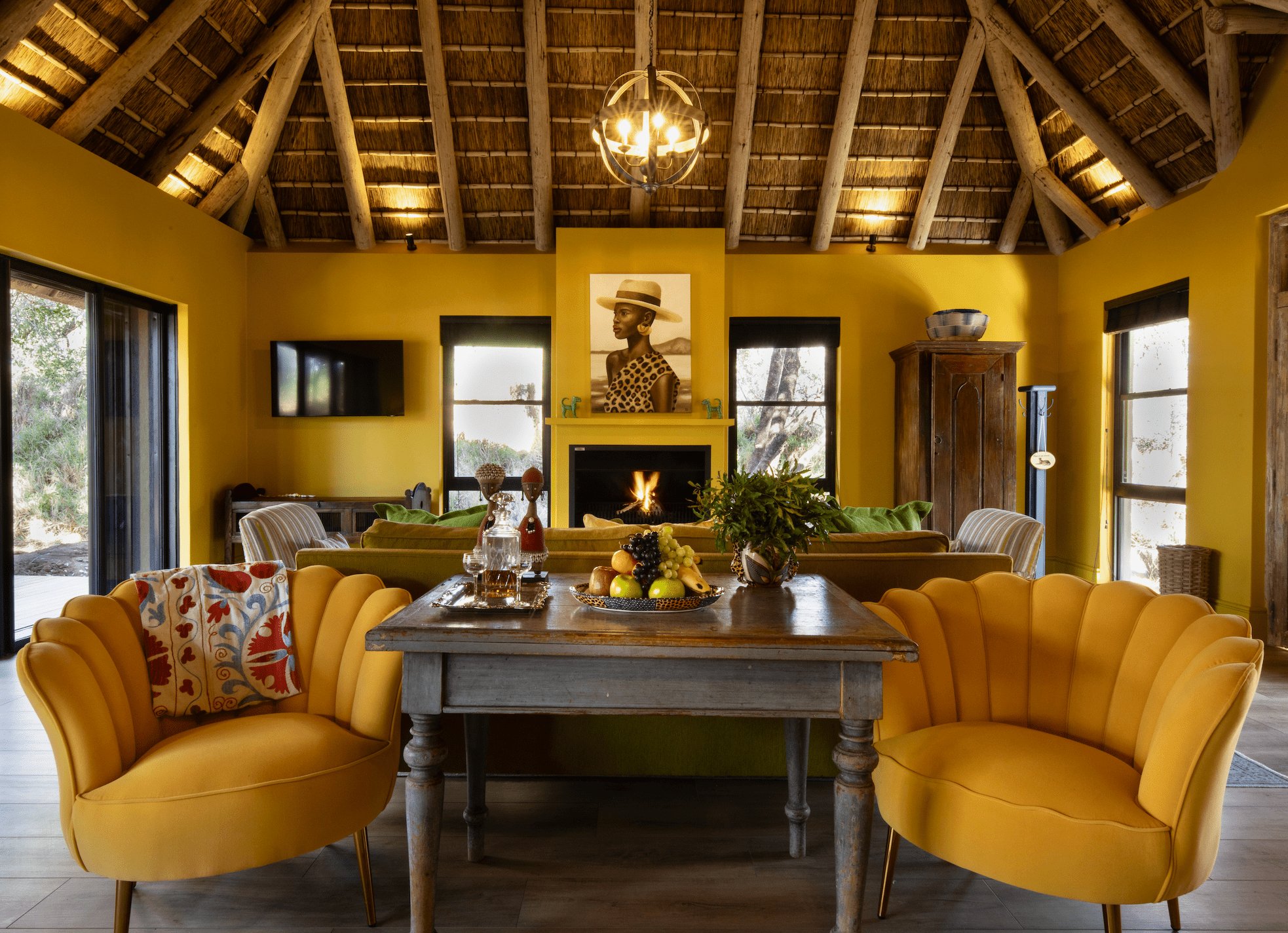 Golden mustard walls and a traditional thatched ceiling create an intimate gathering space, where plush velvet chairs invite lingering conversations by the crackling fireplace.