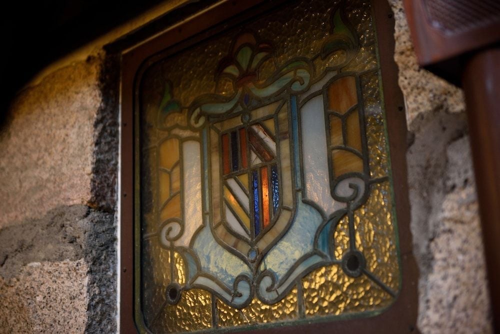 Hand-painted heraldic crests and flowing ribbons adorn stained glass panels, where golden light filters through centuries-old craftsmanship in this intimate corner.