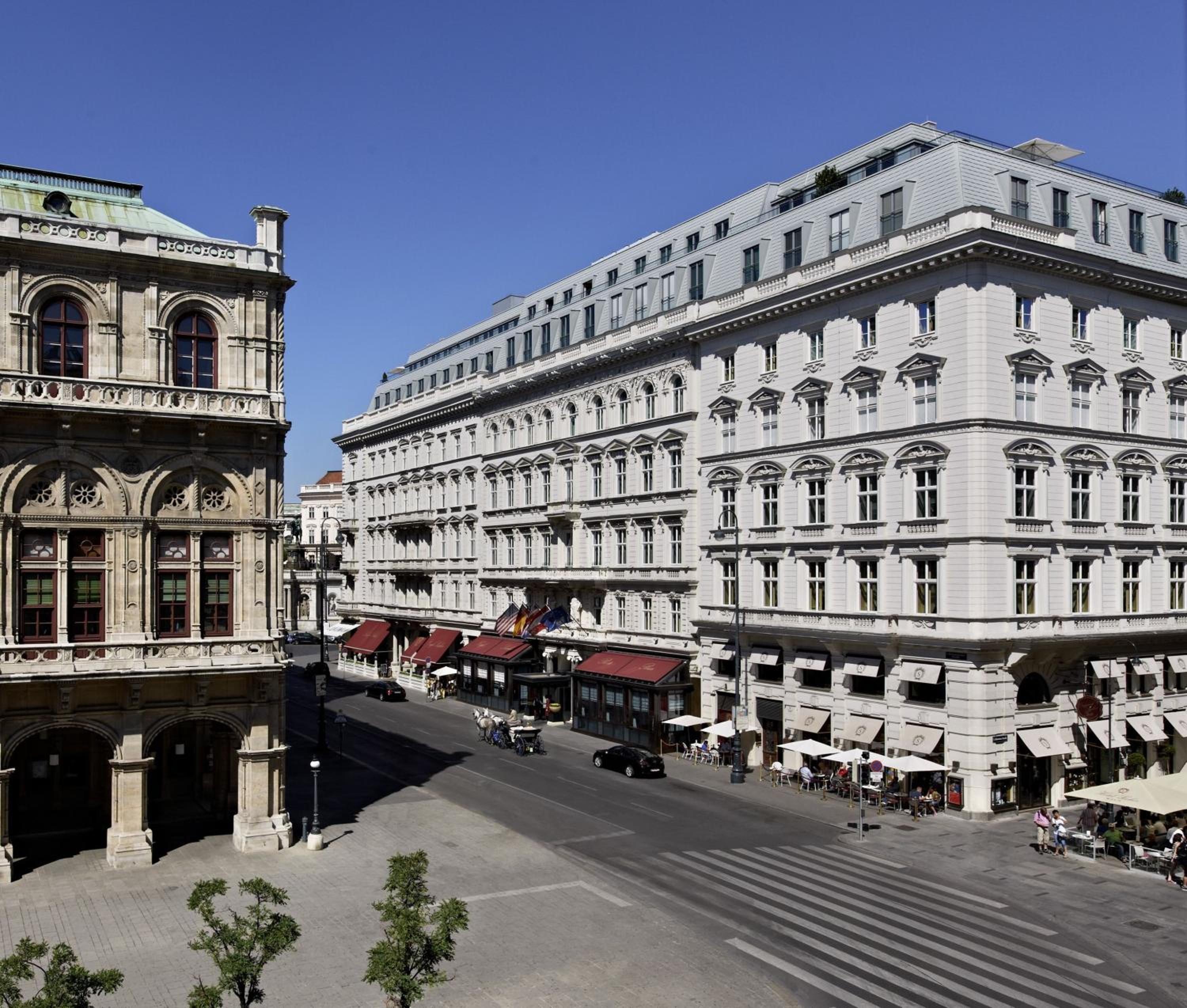Grand Hapsburg-era facades frame the elegant square where Hotel Sacher's guests emerge into Vienna's storied heart, beneath azure skies and centuries of imperial history.