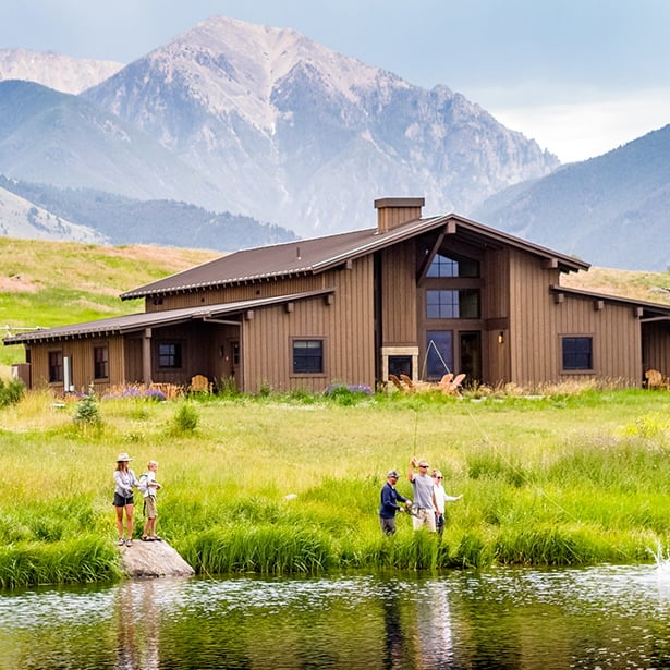 Rustic timber siding and mountain vistas create perfect harmony as guests cast lines into pristine waters steps from their Montana retreat.