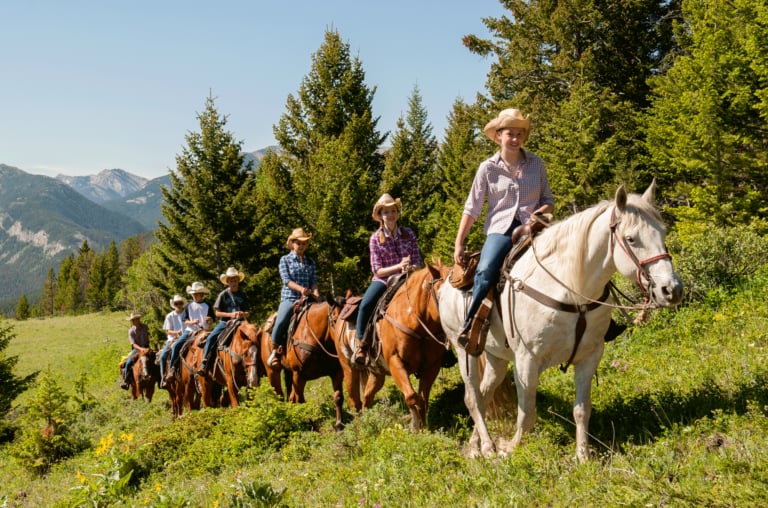 Trail riders wind through alpine meadows dotted with wildflowers, the Gallatin Range providing a dramatic backdrop for authentic Montana horseback adventures.
