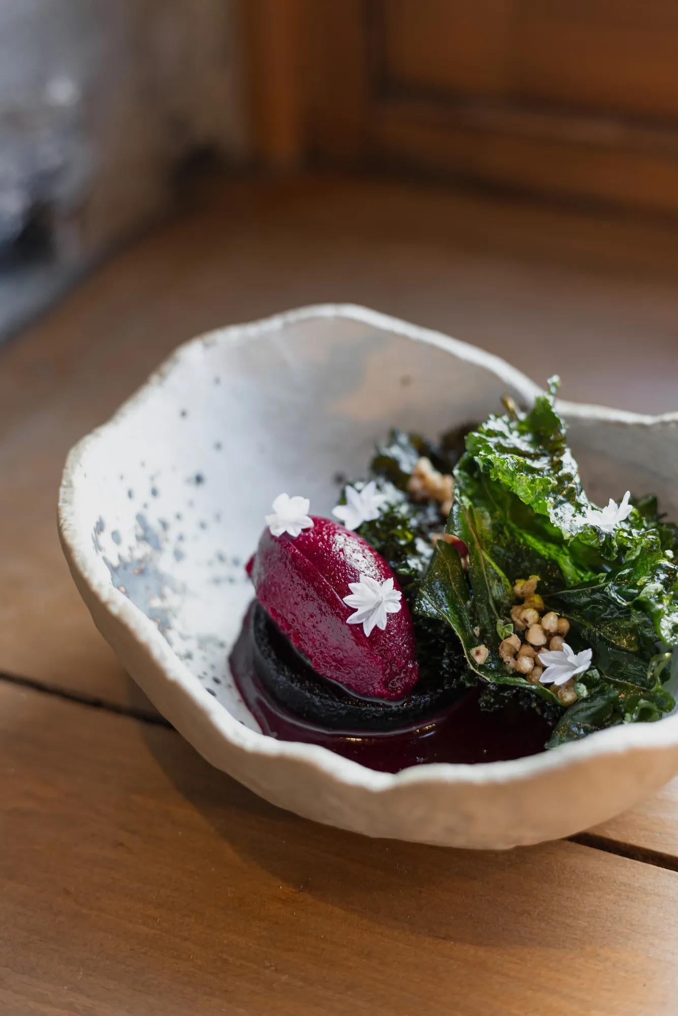 Artfully plated beetroot adorned with delicate white flowers arrives in handcrafted ceramic, showcasing the kitchen's commitment to seasonal Quebec ingredients and precise presentation.