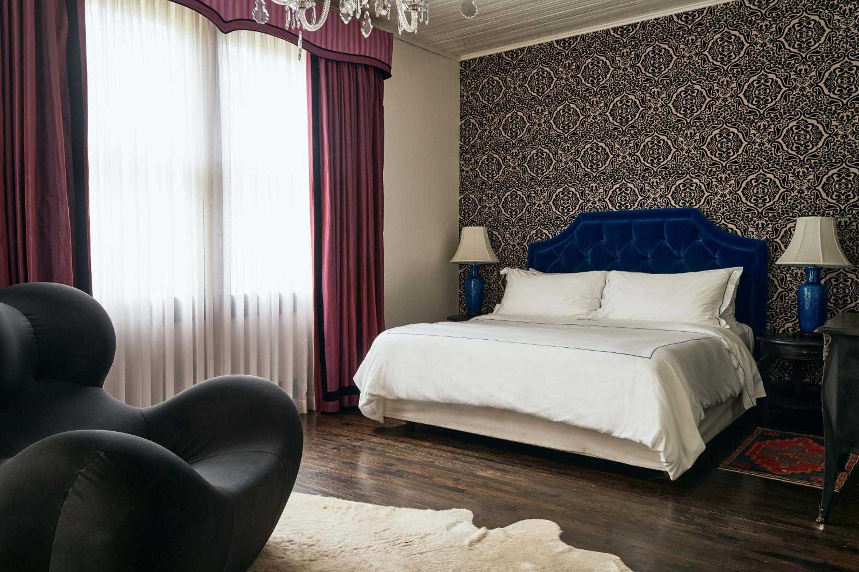 Jewel-toned velvet headboards and ornate wallpaper create an intimate bohemian sanctuary where crystal chandeliers cast warm shadows across polished hardwood floors.