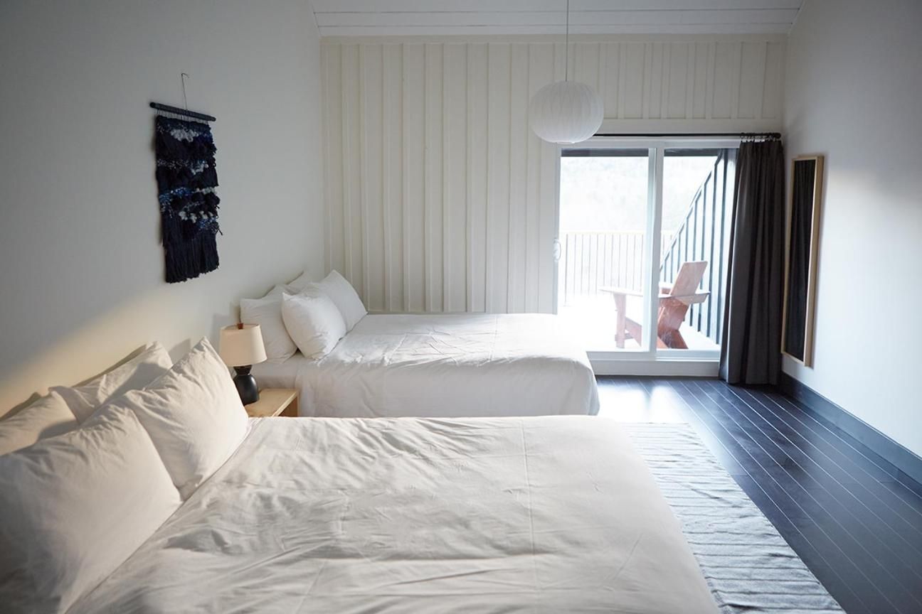Crisp white linens and charcoal curtains create serene contrast in twin-bedded rooms, where private balconies frame mountain views through floor-to-ceiling windows.