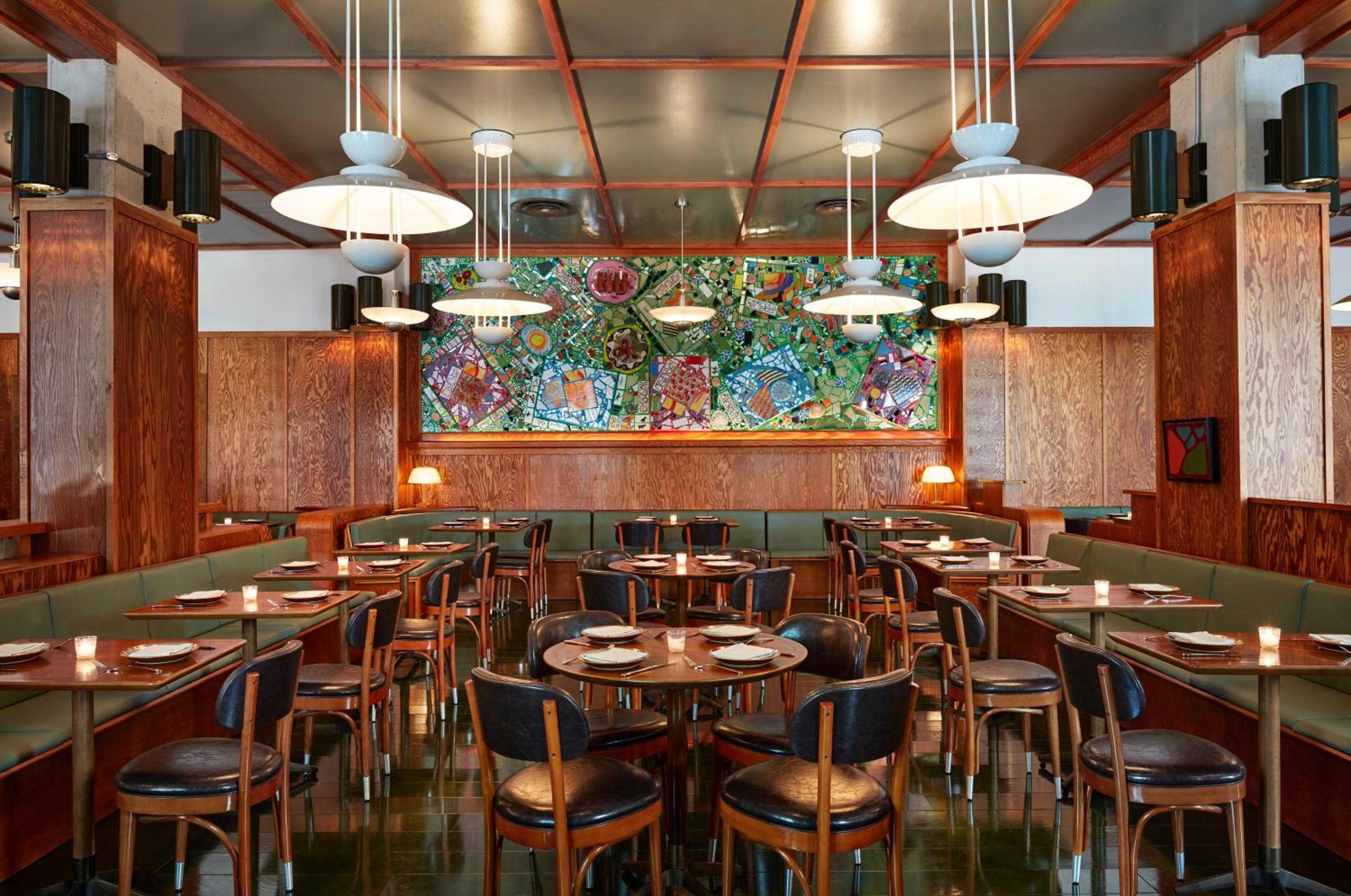 Warm wood paneling and vibrant mosaic artwork create an intimate dining atmosphere, where pendant lights cast a golden glow over perfectly set tables awaiting evening guests.