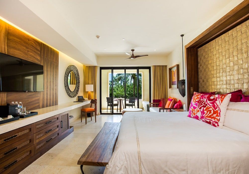Warm wood textures and woven palm headboards create intimate sophistication, while vibrant coral pillows pop against crisp linens in this thoughtfully designed oceanview suite.