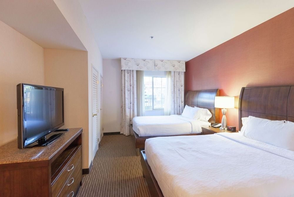 Warm coral accent walls and rich wood furnishings create an inviting retreat, where crisp white linens on twin beds promise restful nights in this thoughtfully designed guest room.