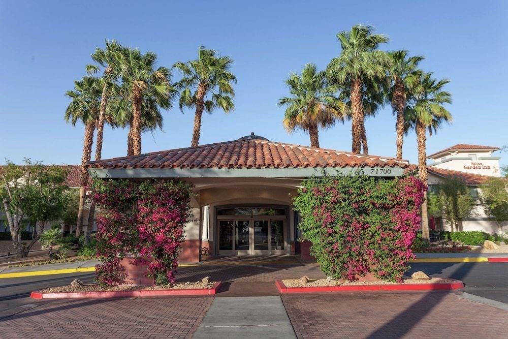 Vibrant bougainvillea cascades across terra cotta walls while towering palms frame the welcoming entrance, creating an oasis-like first impression beneath desert skies.