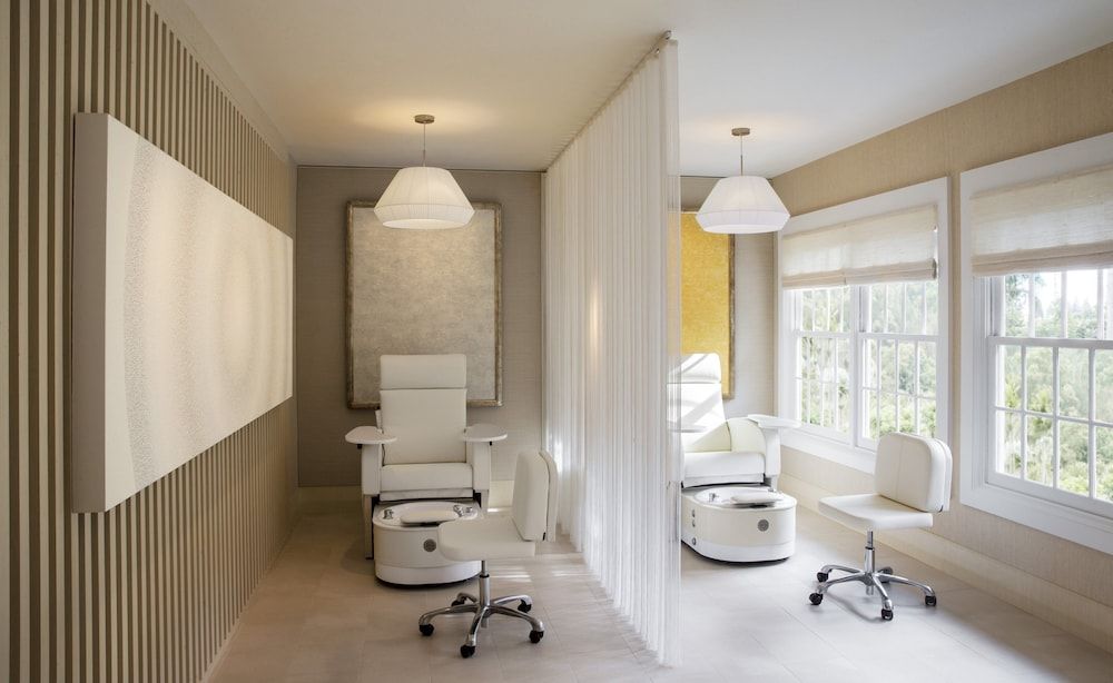 Soft white curtains divide tranquil pedicure stations where natural light streams through floor-to-ceiling windows, creating an intimate sanctuary for wellness rituals.