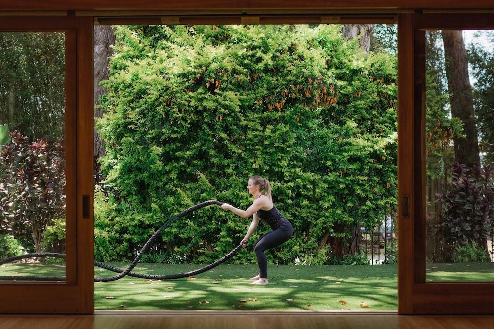 Battle ropes workout sessions unfold beneath towering ironwood trees, where dappled sunlight filters through leaves onto manicured lawns in this serene outdoor fitness sanctuary.