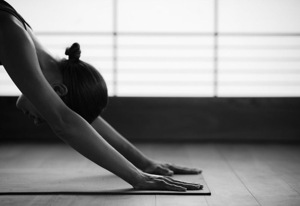 Soft natural light filters through geometric windows as hands find their grounding on yoga mats, creating moments of mindful movement in this serene wellness sanctuary.
