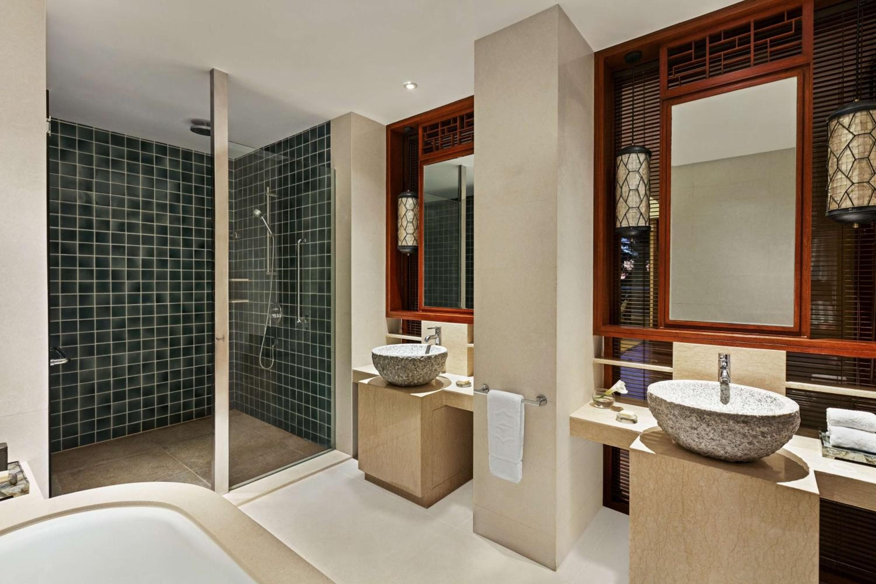 Natural stone vessel sinks and rich teak frames create an open-air sanctuary where tropical breezes flow through thoughtfully designed dual vanities and rain shower.