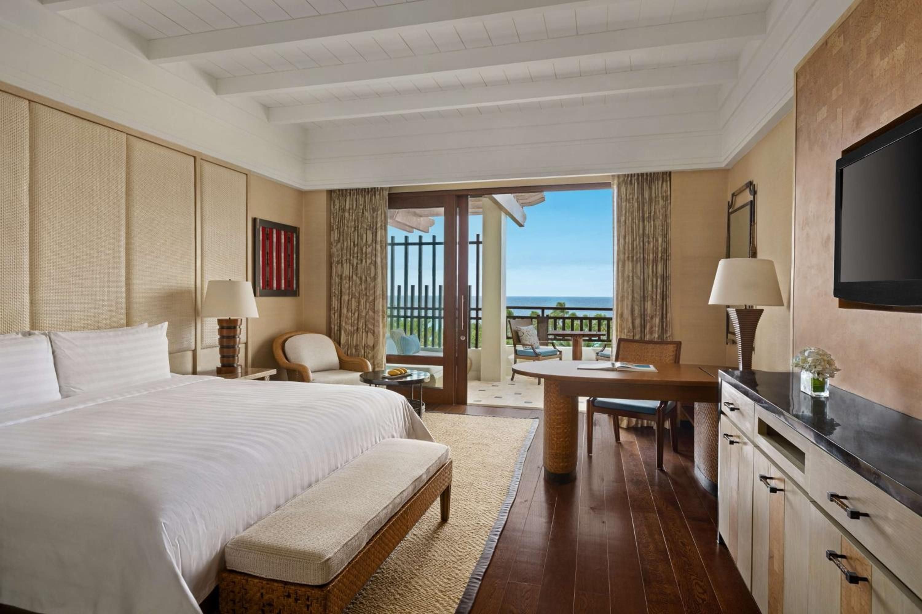 Natural textures and warm wood tones create an elegant retreat, while French doors frame endless ocean views from this thoughtfully appointed guest room.