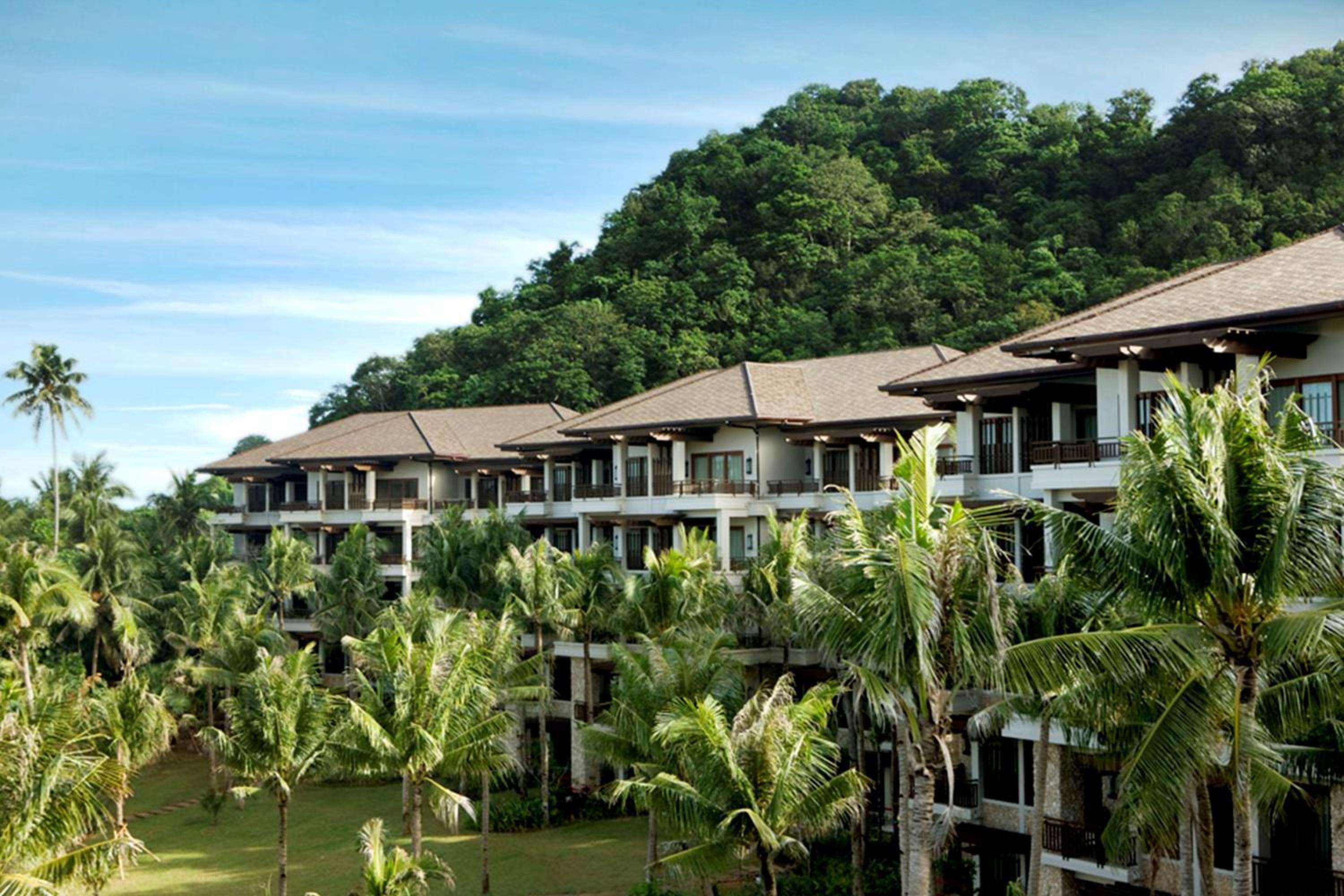 Terraced suites cascade down lush hillsides, their private balconies framed by swaying coconut palms and dense tropical foliage beneath Boracay's endless blue sky.