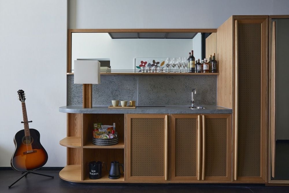 Warm wood cabinetry and speckled stone surfaces create an intimate bar corner where craft cocktails meet minimalist Japanese design sensibilities.