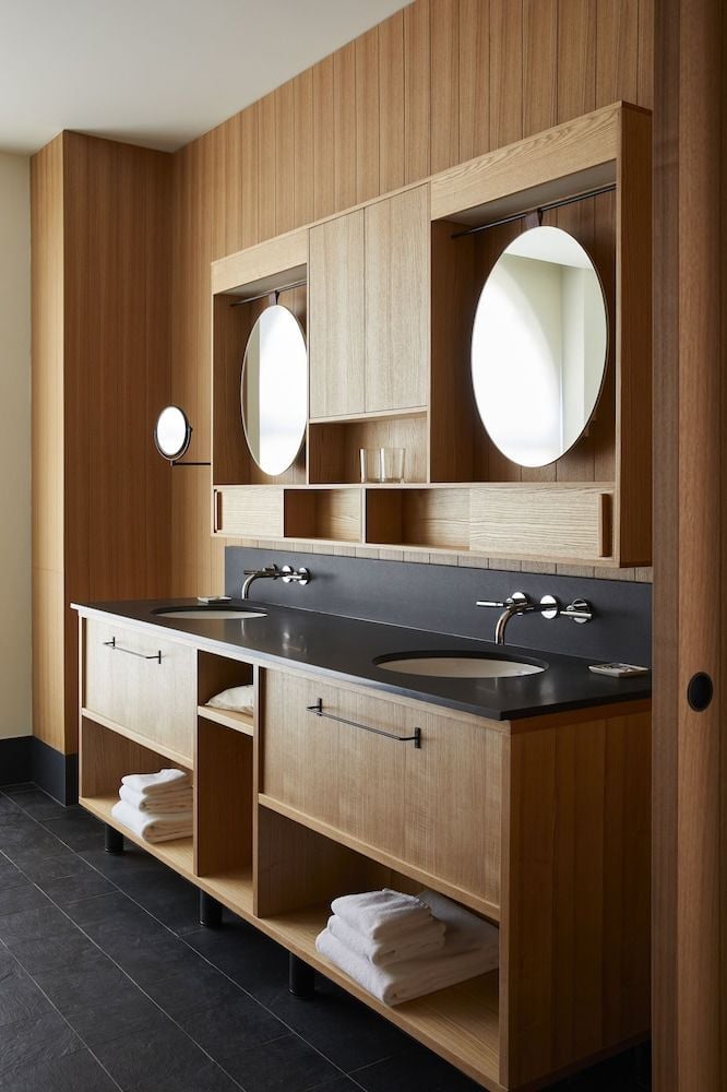 Warm oak cabinetry and sleek black stone create a serene double vanity, where circular mirrors catch soft light filtering through this thoughtfully crafted washroom.