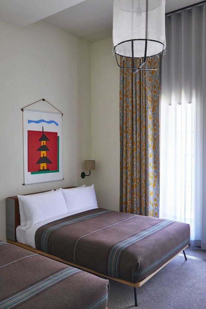 Whimsical patterned curtains frame the structural column while bold artwork depicting a traditional pagoda adds playful contrast to minimalist bedding and mid-century furnishings.