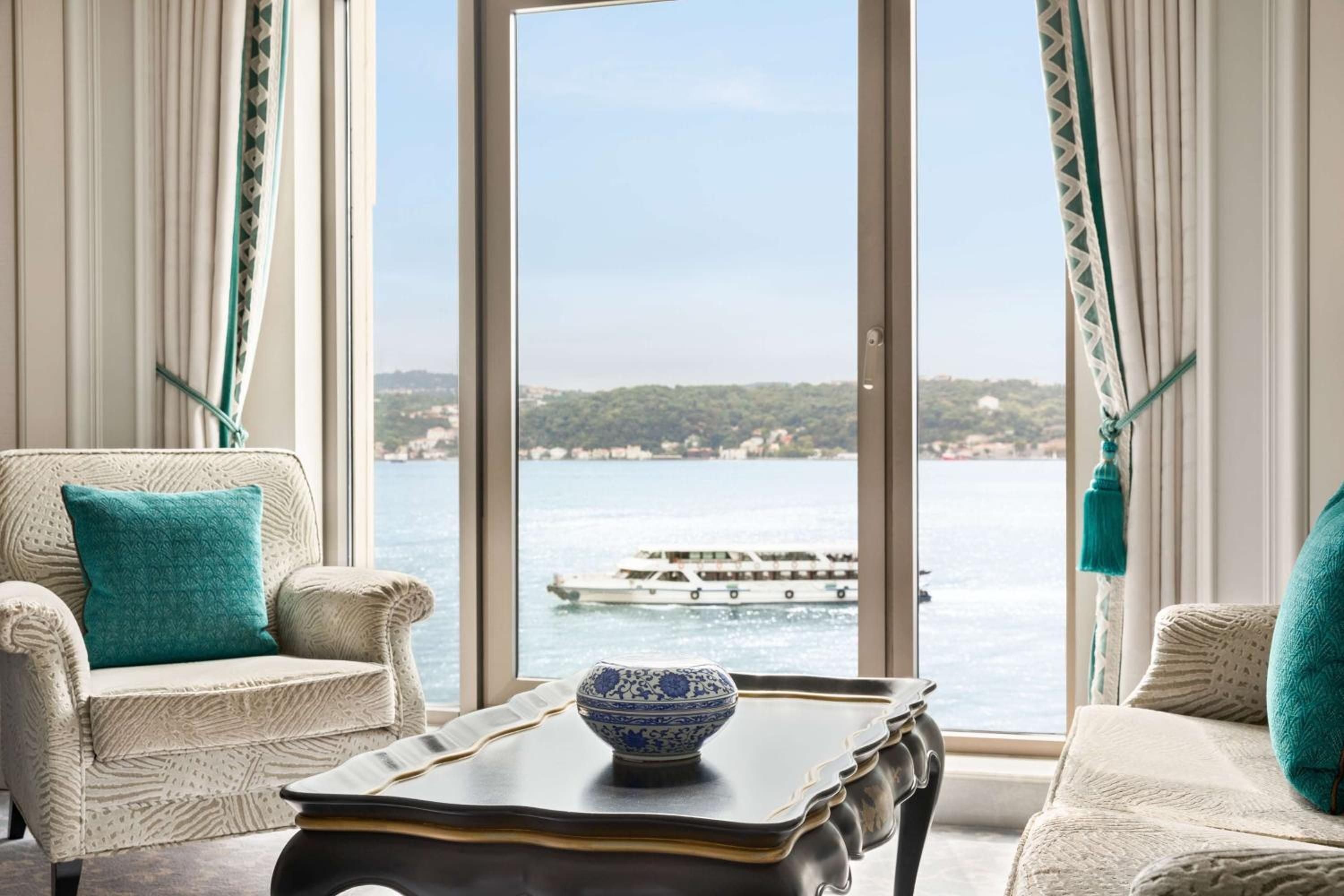 Nautical-inspired textiles and azure accents frame panoramic Bosphorus views from this elegantly appointed suite, where luxury yachts drift past forested shores like floating dreams.