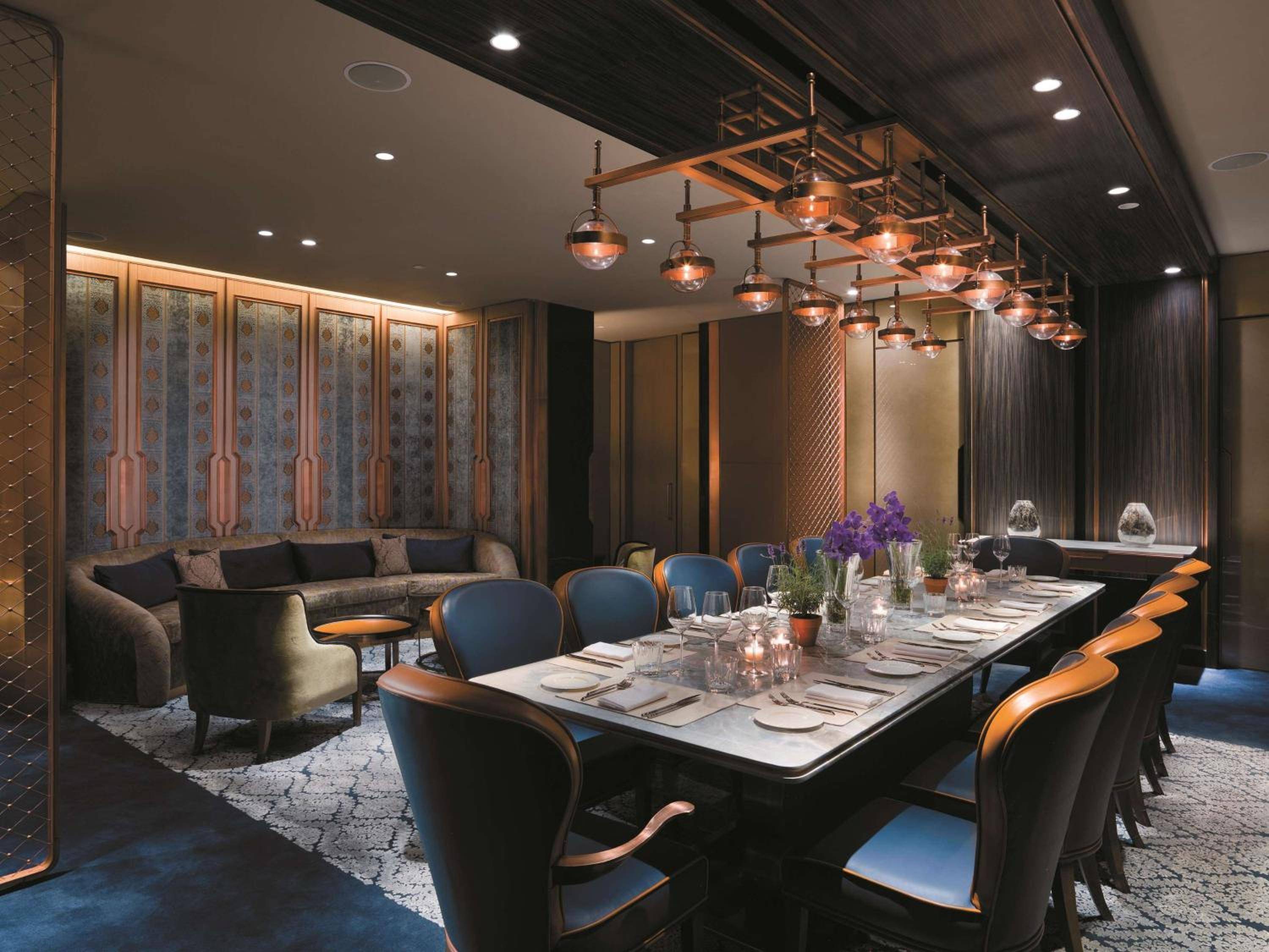 Copper pendant lights cascade over the intimate private dining room, where navy velvet chairs and patterned wallcoverings create an atmosphere of understated luxury and warmth.