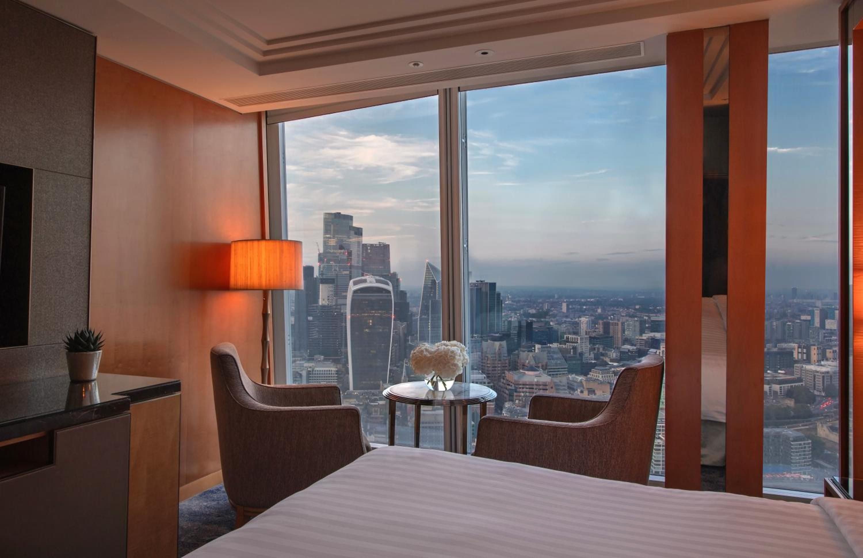 Floor-to-ceiling windows frame London's sprawling cityscape from this elegantly appointed guest room, where warm amber lighting creates an intimate sanctuary high above the Thames.