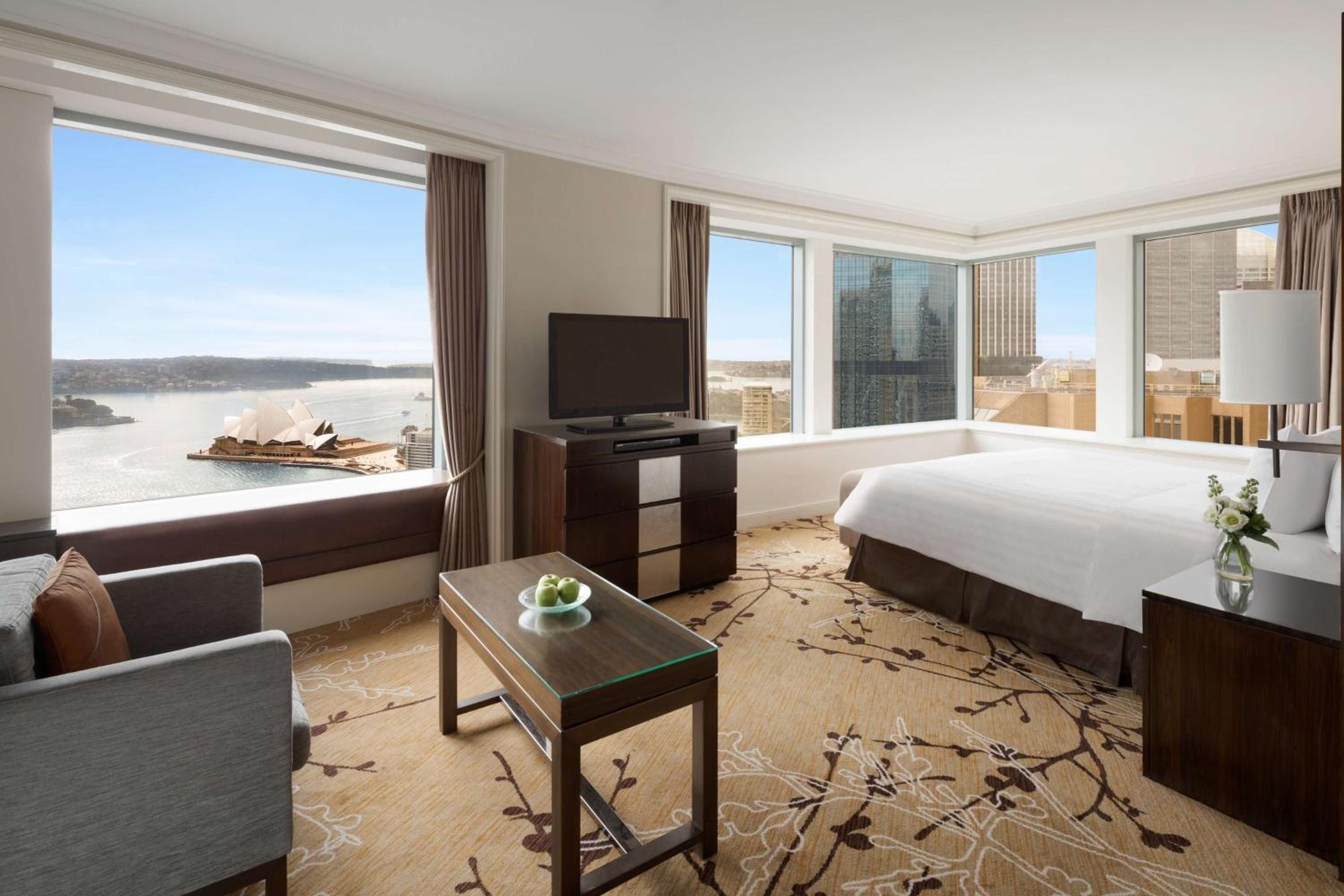 Corner suites frame Sydney Opera House's iconic shells through floor-to-ceiling windows, while warm timber furnishings and botanical carpets create an intimate harbor-view sanctuary.