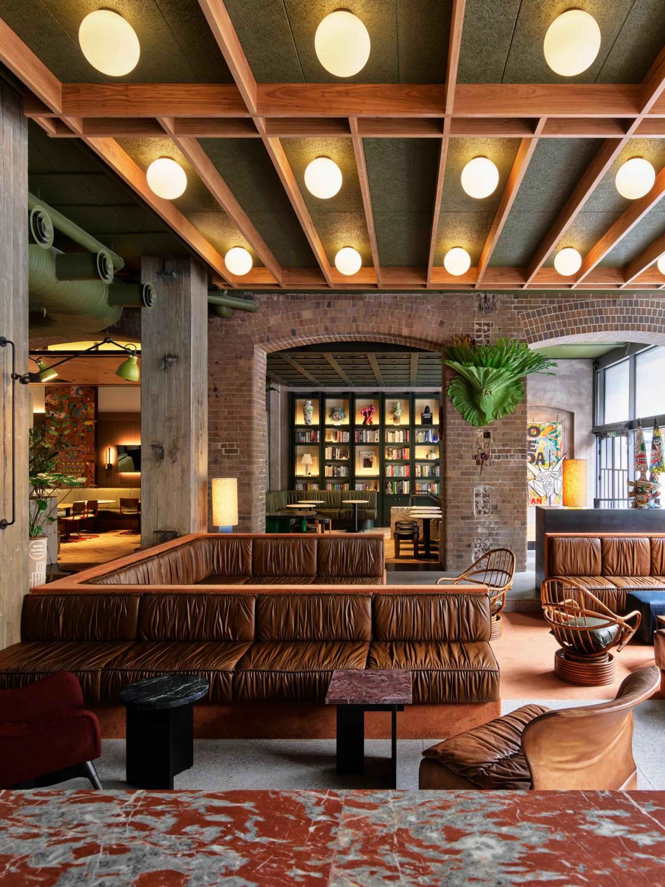 Warm pendant lights cast a golden glow over cognac leather banquettes and exposed brick arches, while vintage rugs anchor this inviting industrial-chic gathering space.