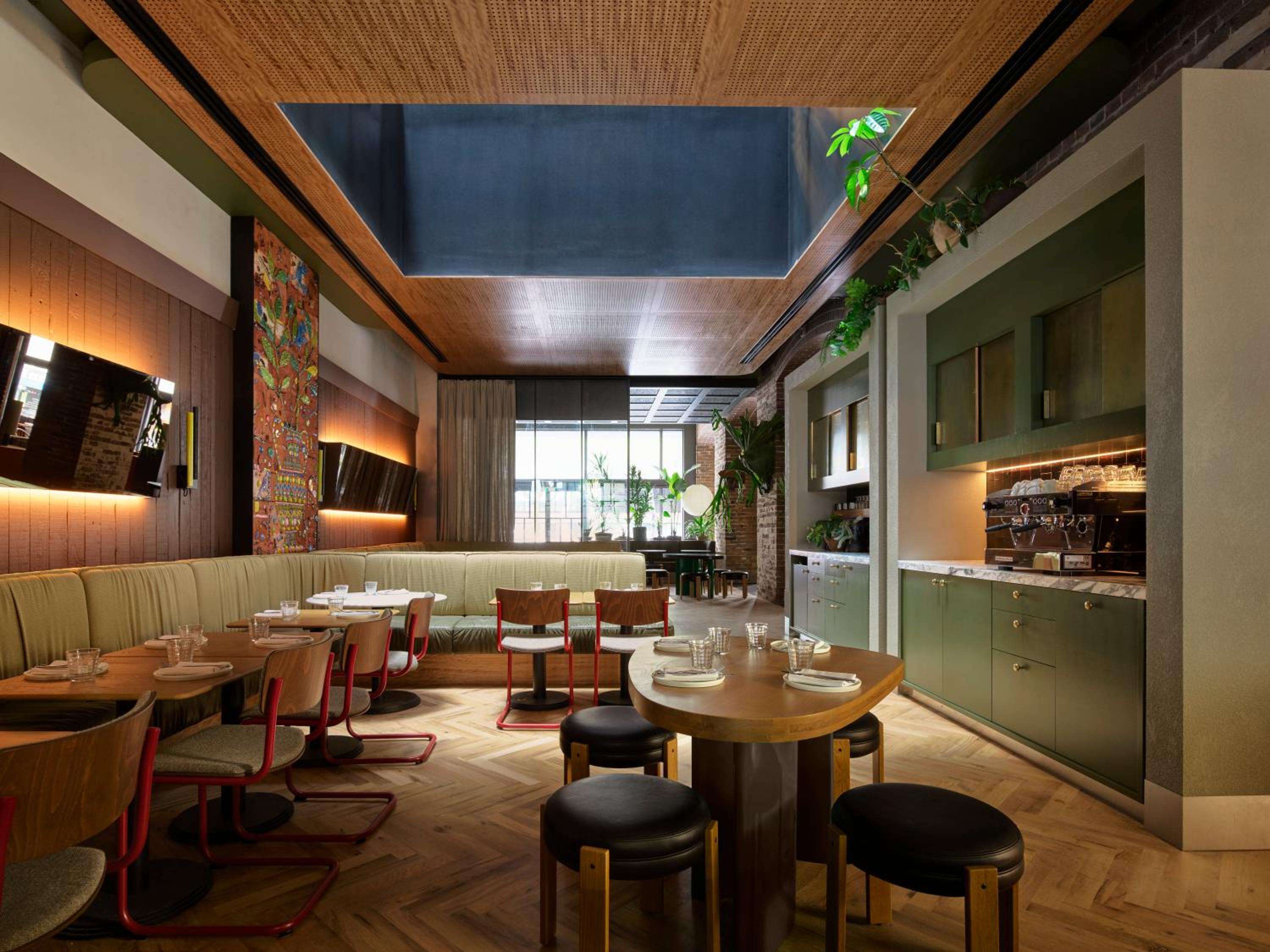Natural light streams through the skylight onto sage-green banquettes and parquet floors, where communal tables invite lingering over locally-sourced plates in this warmly industrial dining space.