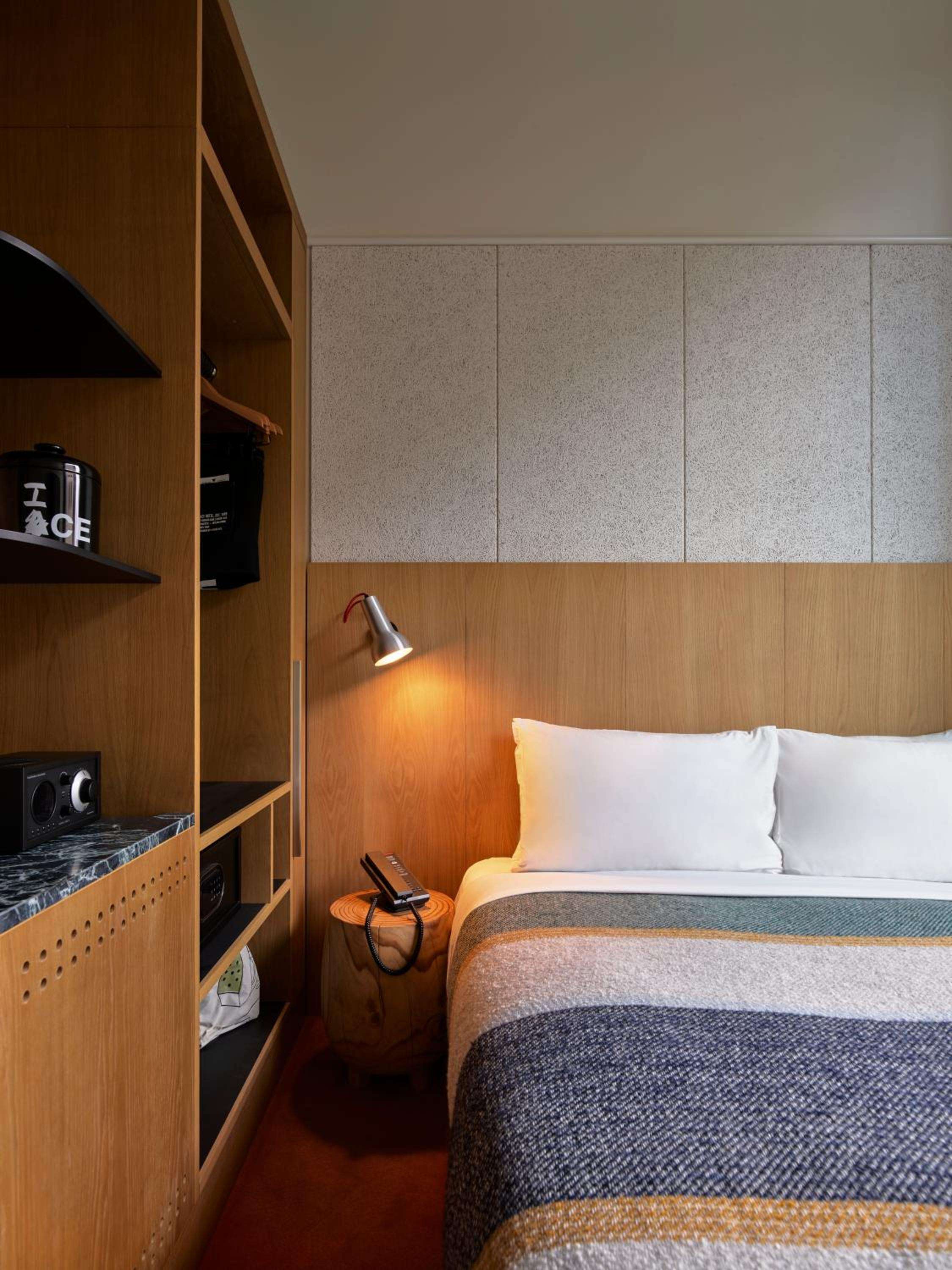 Warm timber shelving houses vintage radios and books beside the bed, while a sleek reading light casts intimate pools of golden light across textured linens.