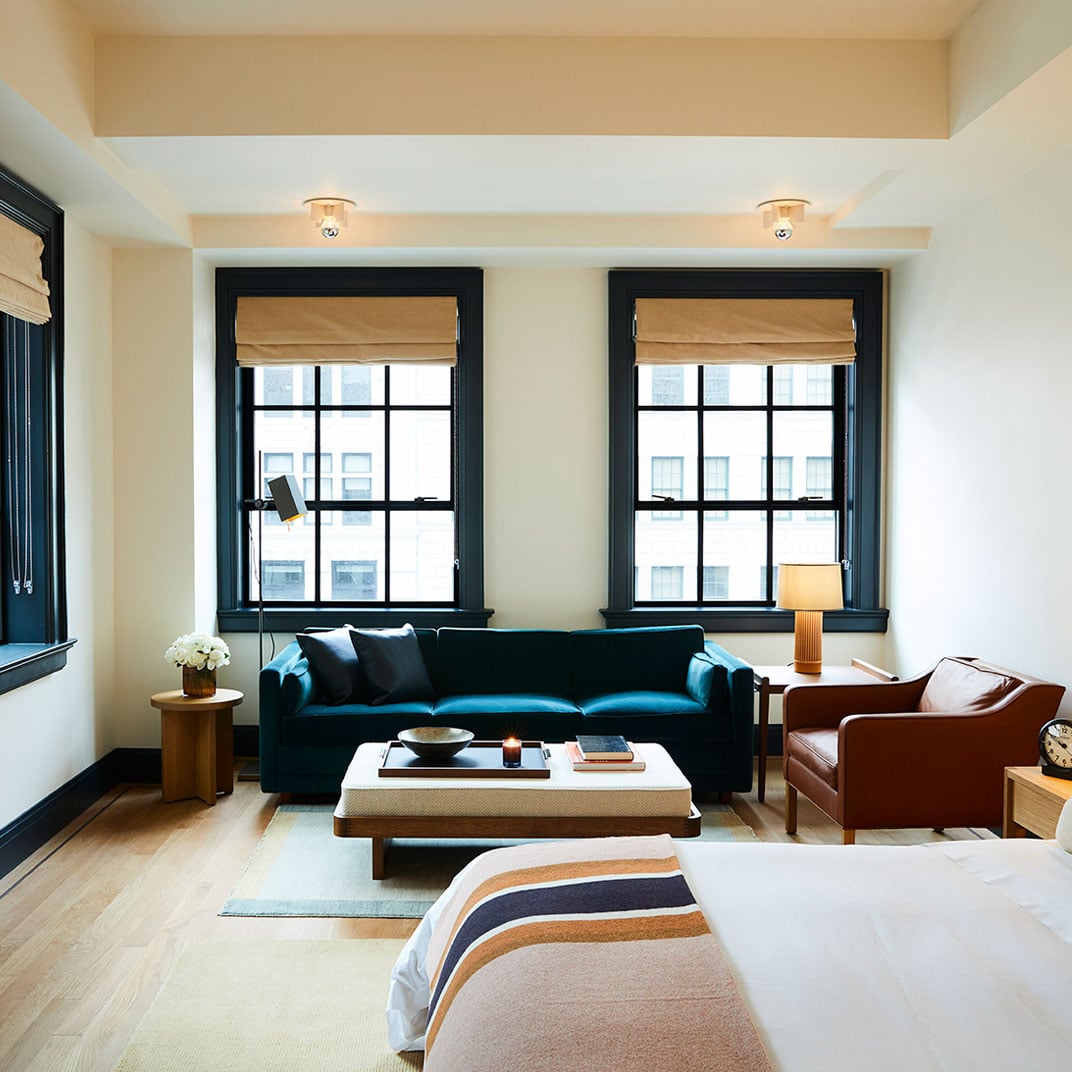 Rich navy velvet meets warm cognac leather in thoughtfully designed suites where black-framed windows frame Detroit's architectural heritage beyond striped throws.