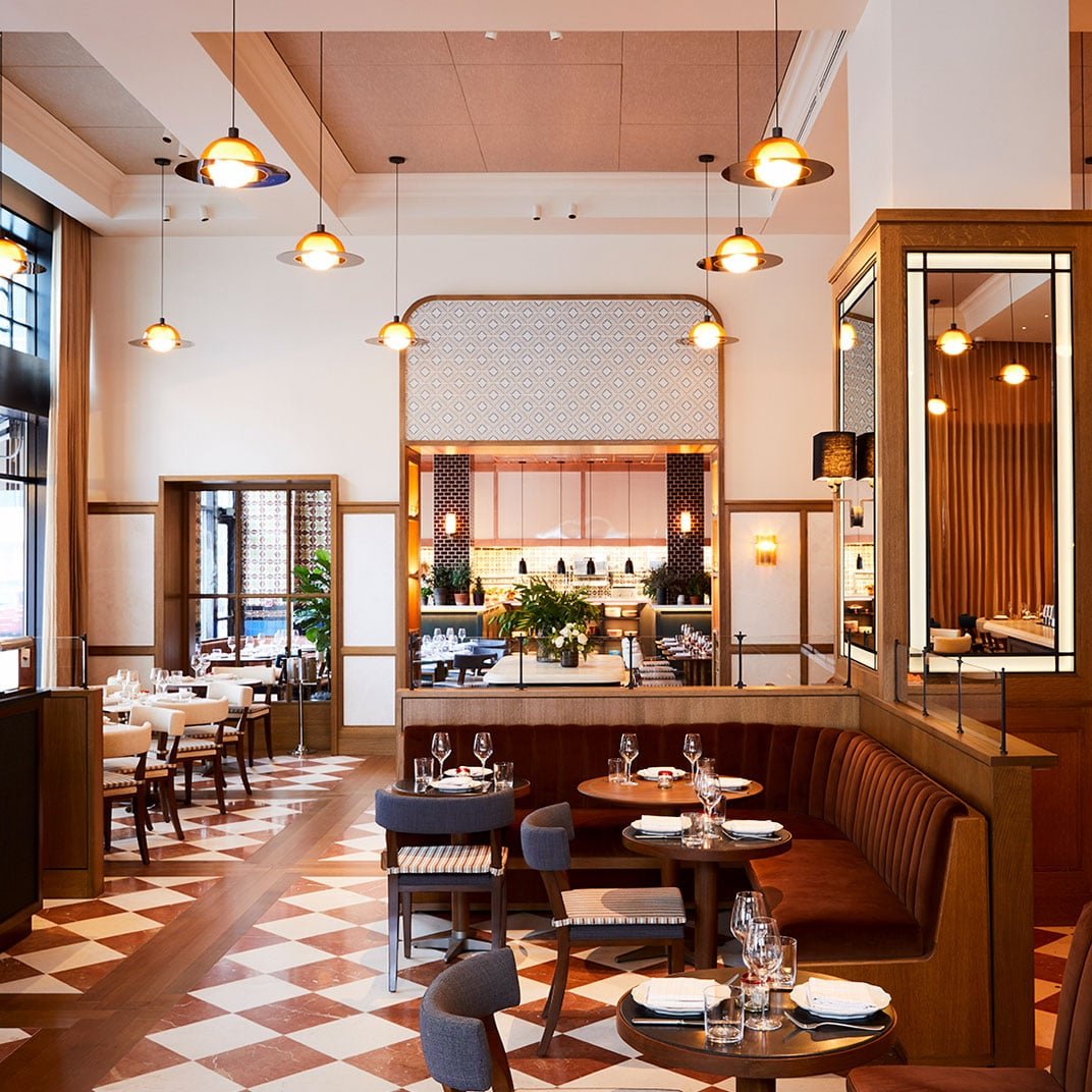 Warm pendant lights cast a golden glow over rich leather banquettes and geometric tile floors, creating an inviting atmosphere where modern comfort meets timeless design.
