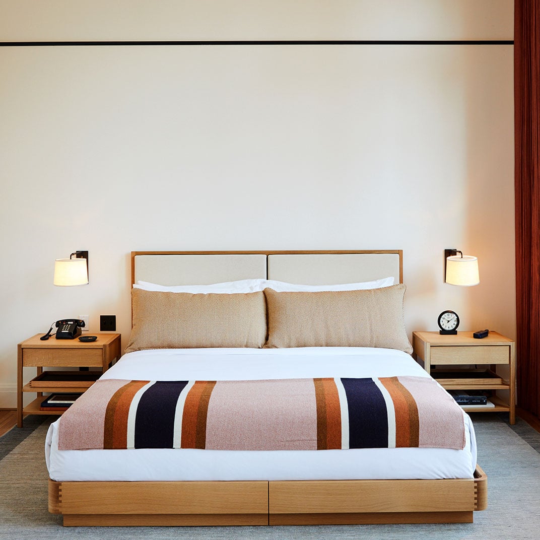 Clean lines and warm wood tones define guest rooms, where striped throws in rust and navy add artisanal character to minimalist furnishings and thoughtfully curated lighting.