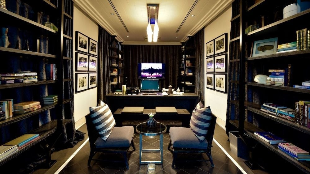 Floor-to-ceiling bookshelves frame intimate seating where guests browse curated volumes while soft lighting illuminates framed photography and carefully arranged artifacts.