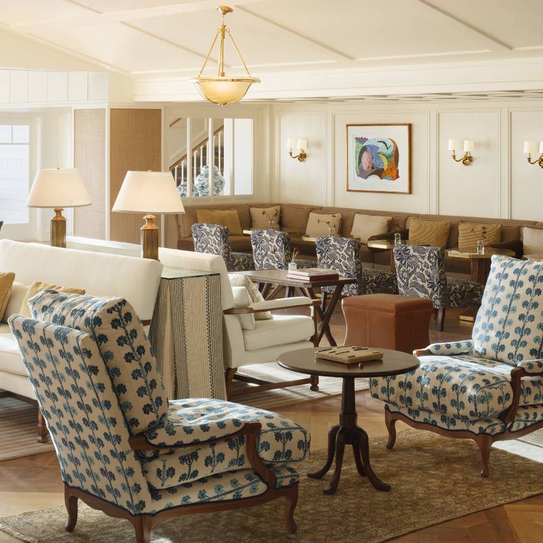 Nautical-inspired armchairs in crisp blue florals anchor this refined common area, where warm wood tones and brass fixtures evoke classic seaside elegance.