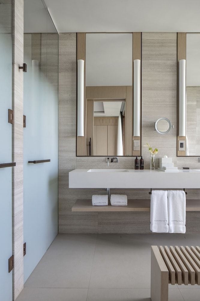 Warm travertine and sleek brass fixtures create a spa-like sanctuary, where natural textures meet contemporary luxury in thoughtfully designed guest bathrooms.