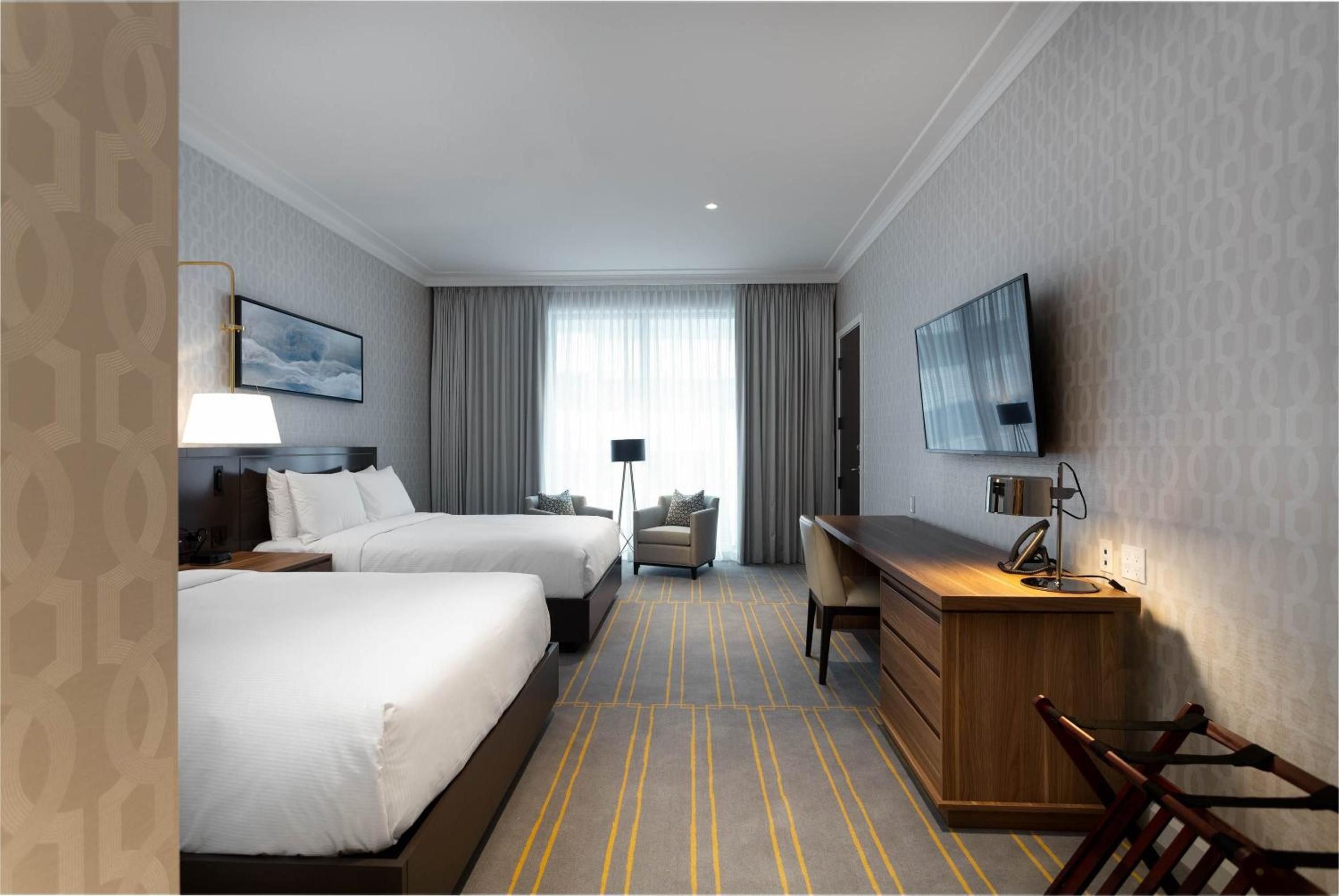 Warm wood tones and crisp linens create an understated elegance in the twin-bedded rooms, where geometric carpet patterns add visual interest beneath soaring ceilings.