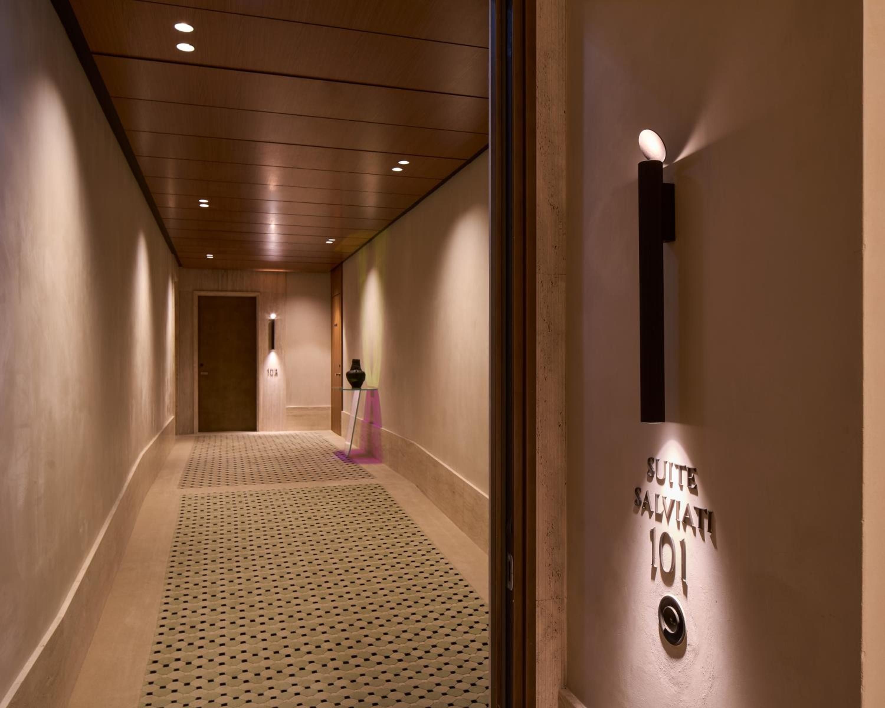 Warm wood ceilings and sophisticated lighting guide guests through serene corridors to Suite Salviati 101, where understated luxury meets contemporary Italian design.
