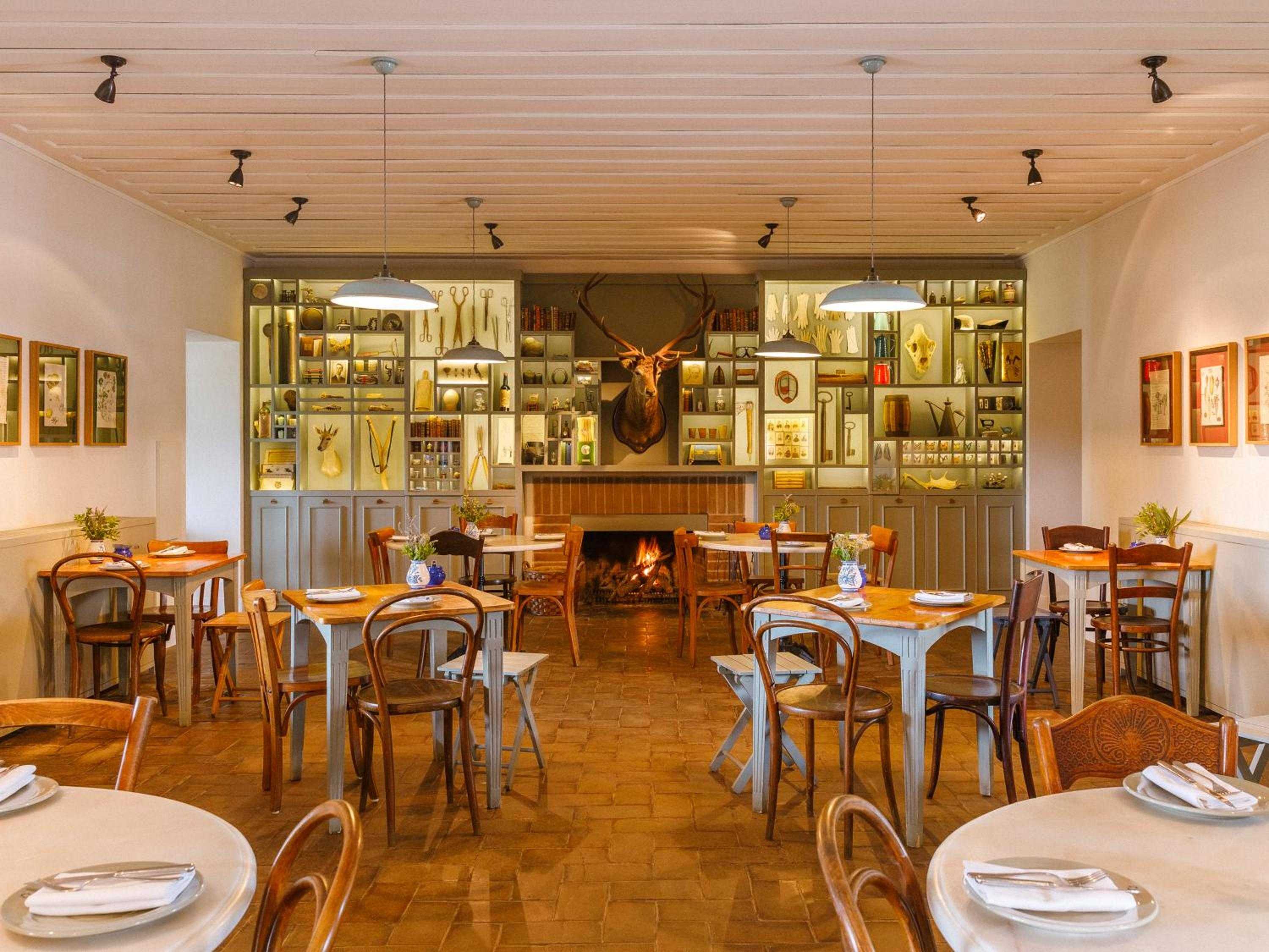 Bentwood chairs and flickering firelight create intimate dining beneath cabinets displaying local curiosities, where rustic Portuguese charm meets contemporary comfort in the estate's restaurant.