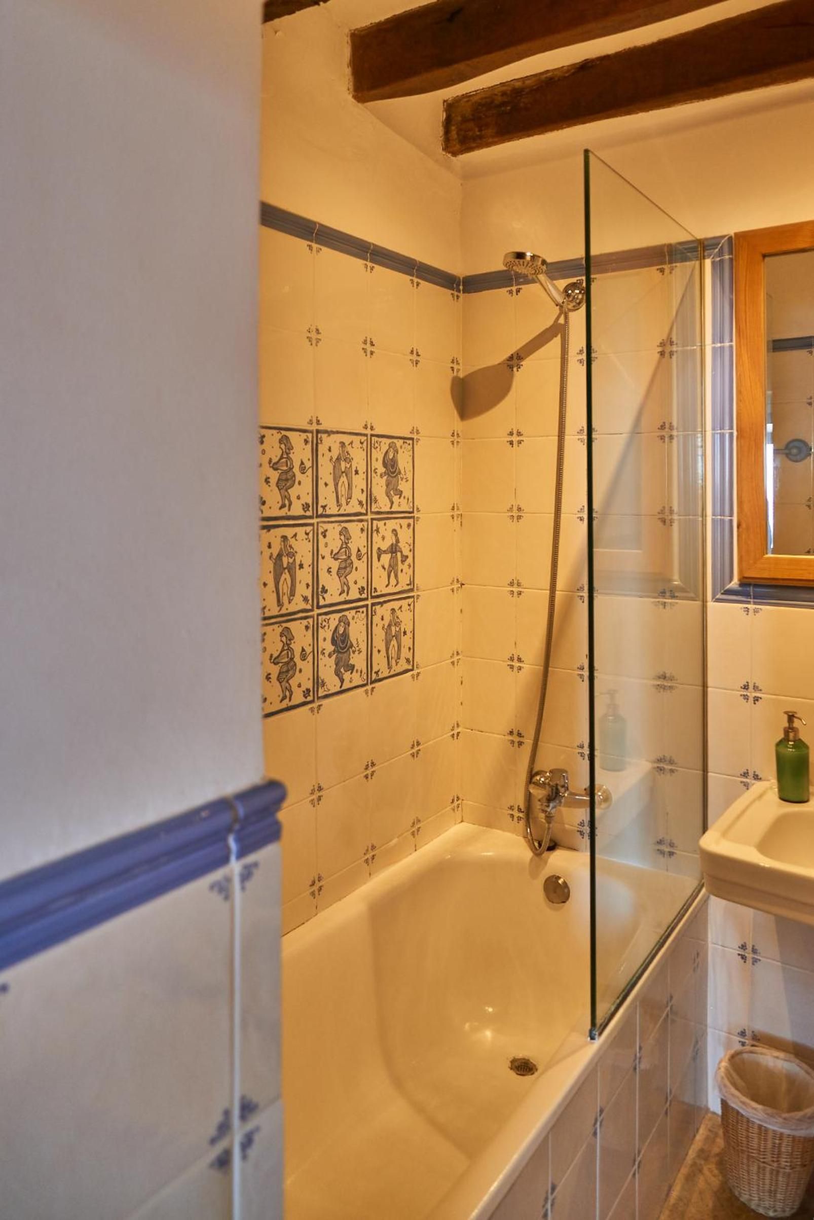 Hand-painted tiles depicting medieval figures transform this intimate bathroom into an artistic retreat, where exposed beams meet contemporary glass and warm candlelight.