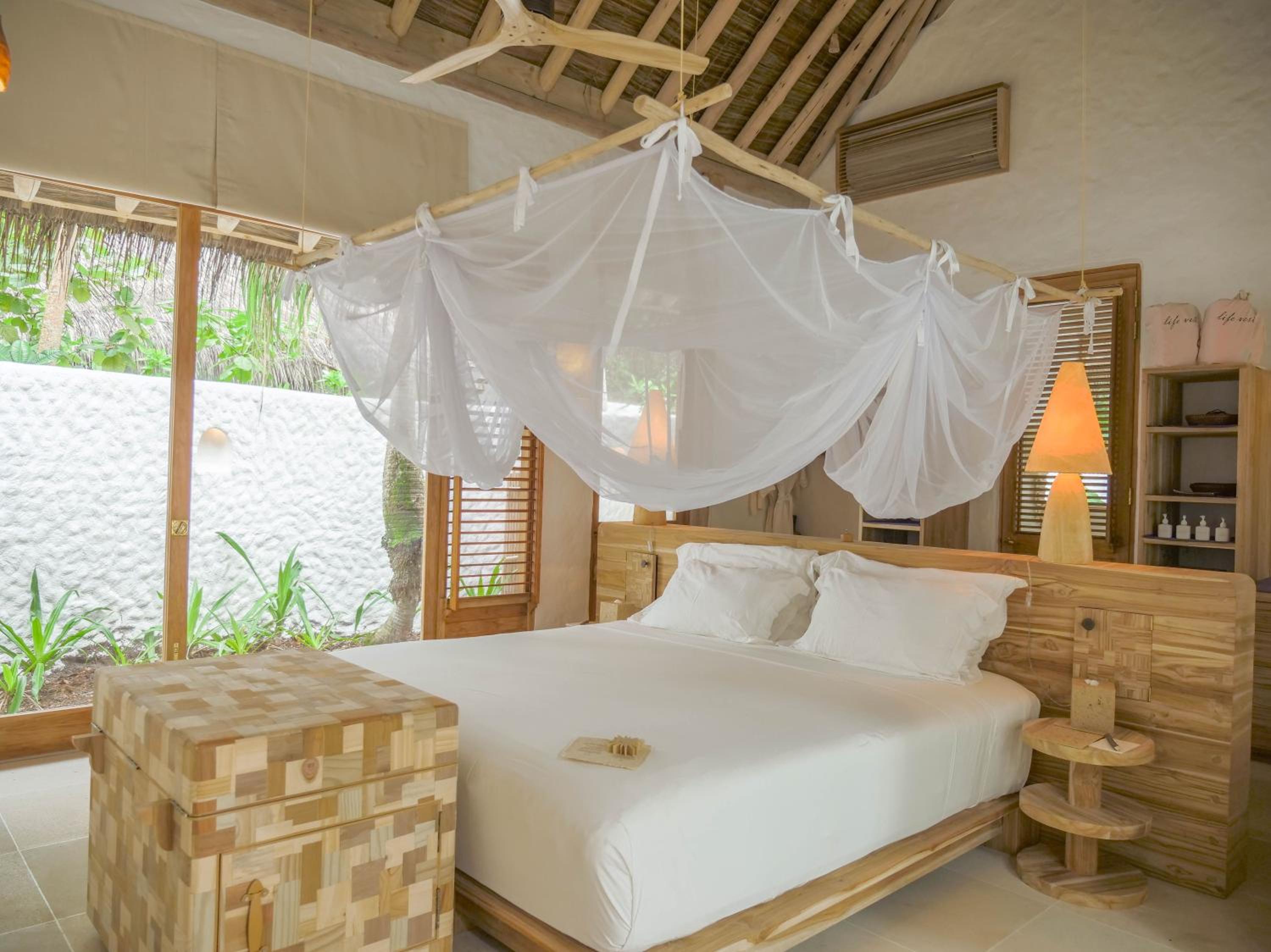 Natural teak furnishings and billowing mosquito nets create an intimate sanctuary where exposed rafters and tropical breezes blur the line between indoors and out.