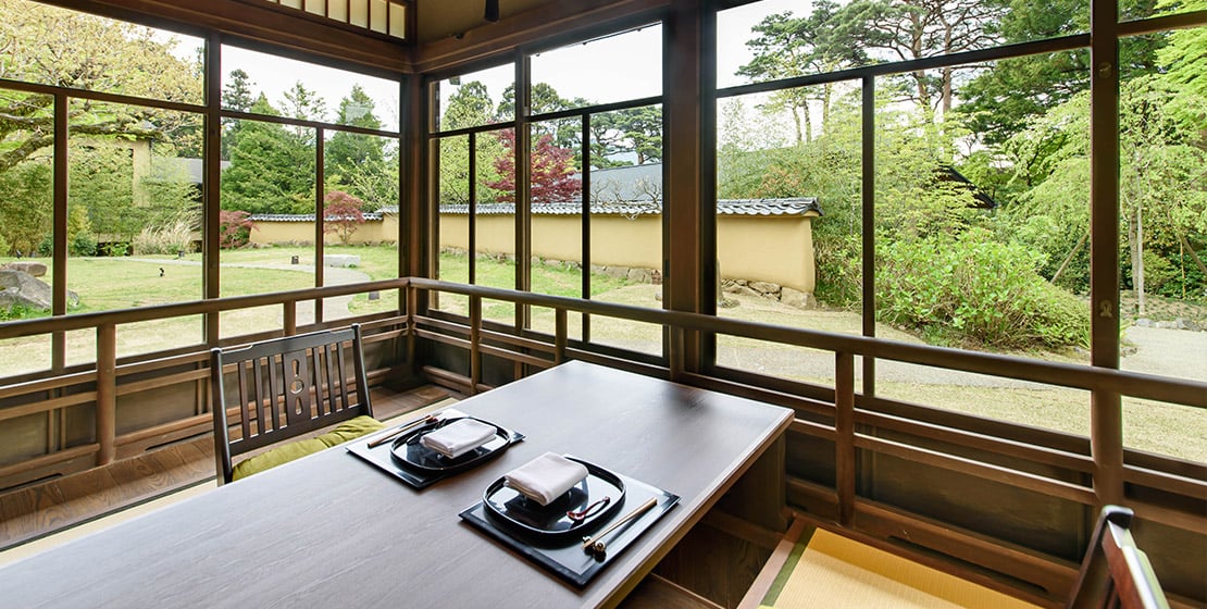 Floor-to-ceiling windows frame verdant Japanese gardens from this serene dining nook, where lacquered trays await the evening's kaiseki ceremony.