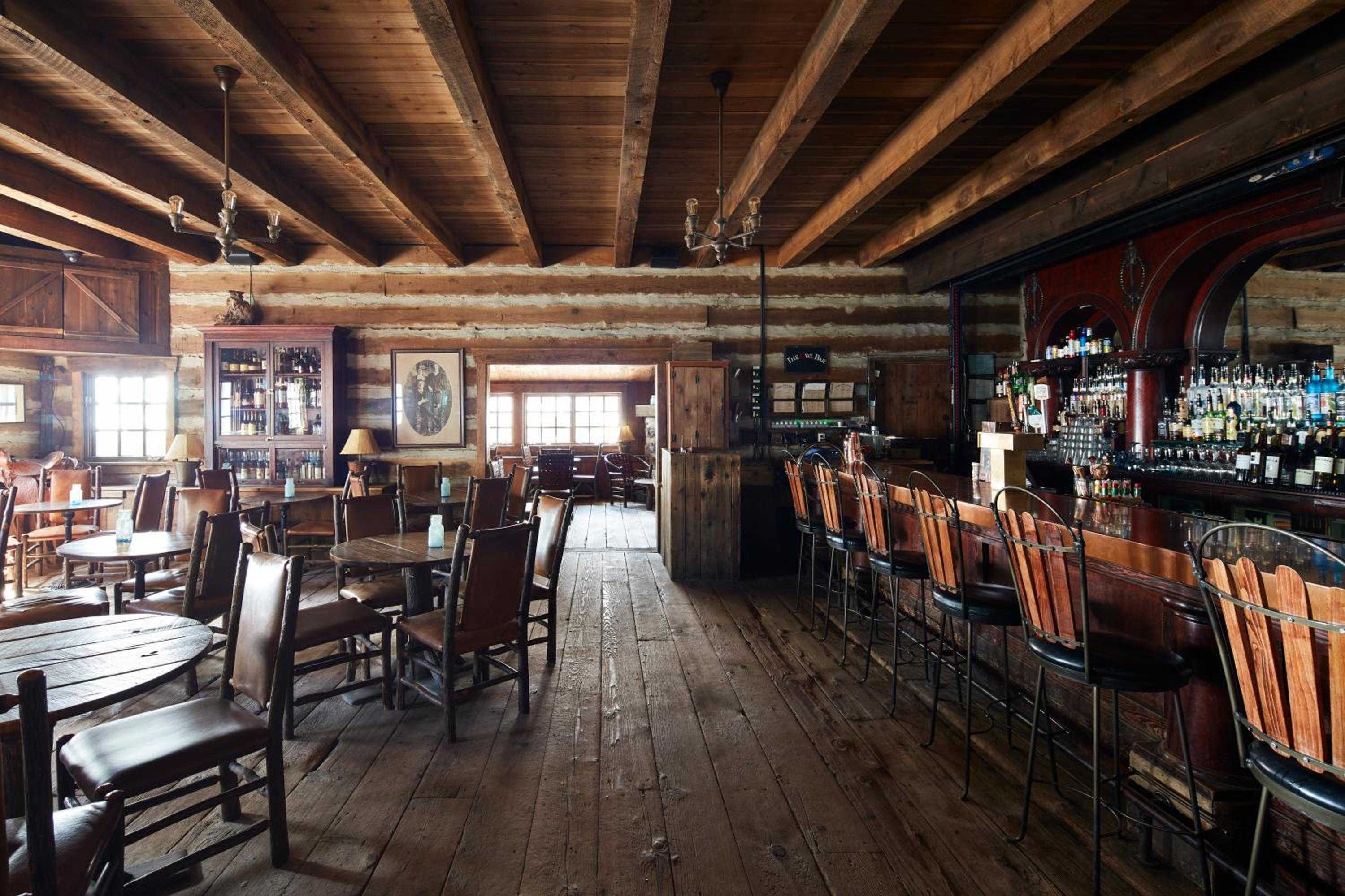 Exposed log beams and weathered plank floors create an authentic mountain saloon atmosphere, where rustic wooden bar stools invite lingering over craft cocktails and local spirits.