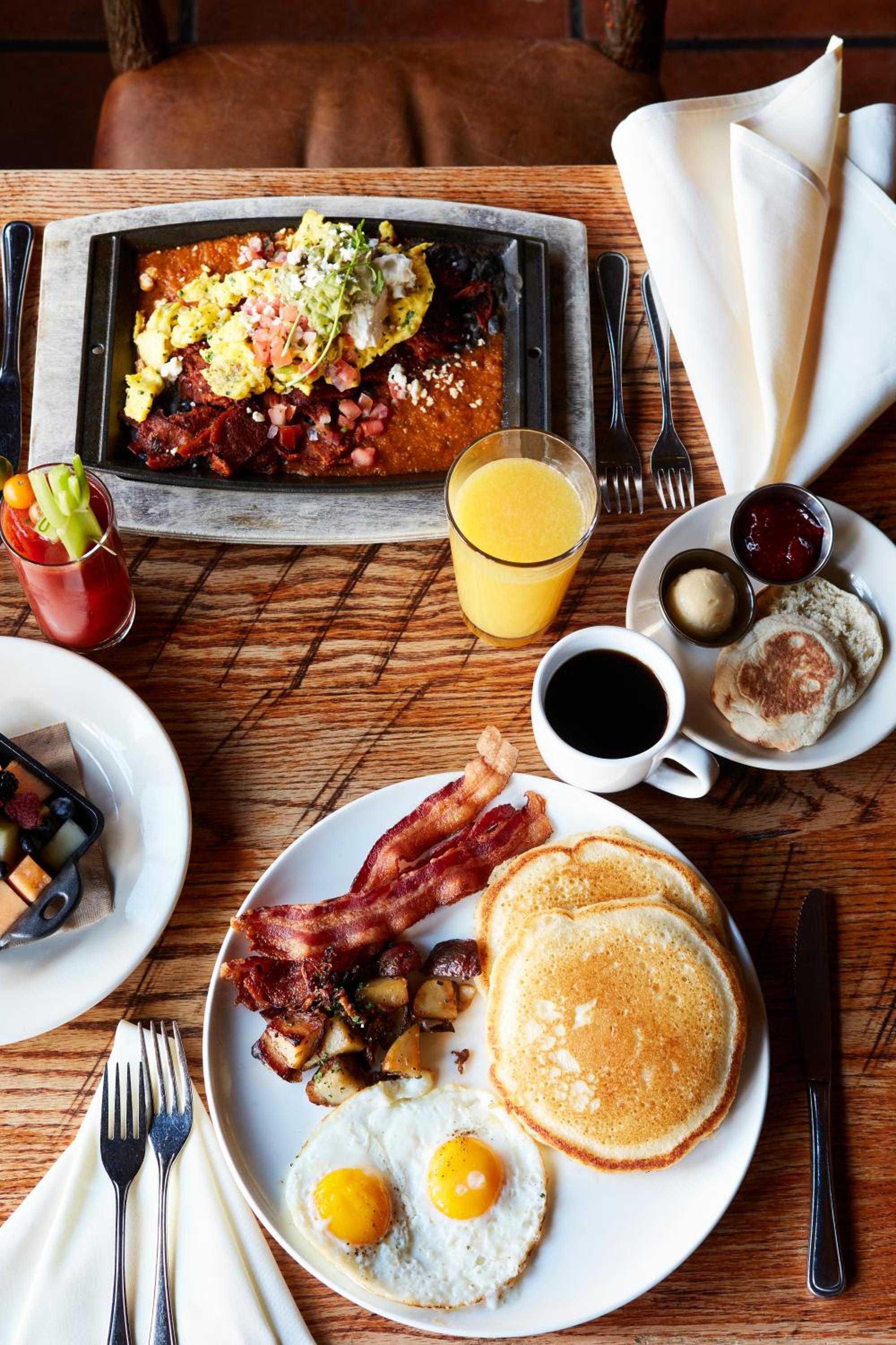 Mountain mornings call for hearty fare: crispy bacon, golden pancakes, and farm-fresh eggs fuel adventures ahead, while rich coffee steams in ceramic mugs.