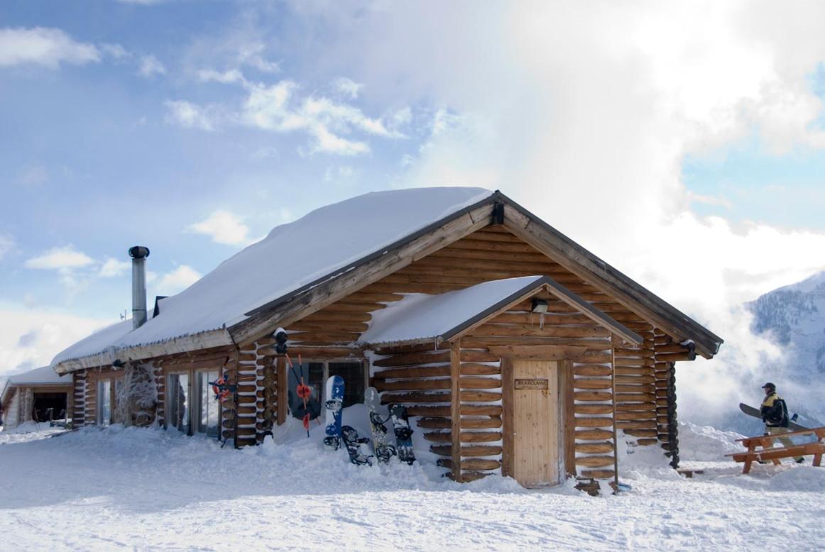 Snow-dusted log cabins nestle against dramatic alpine peaks, where skis lean ready against weathered timber walls and mountain silence speaks louder than words.