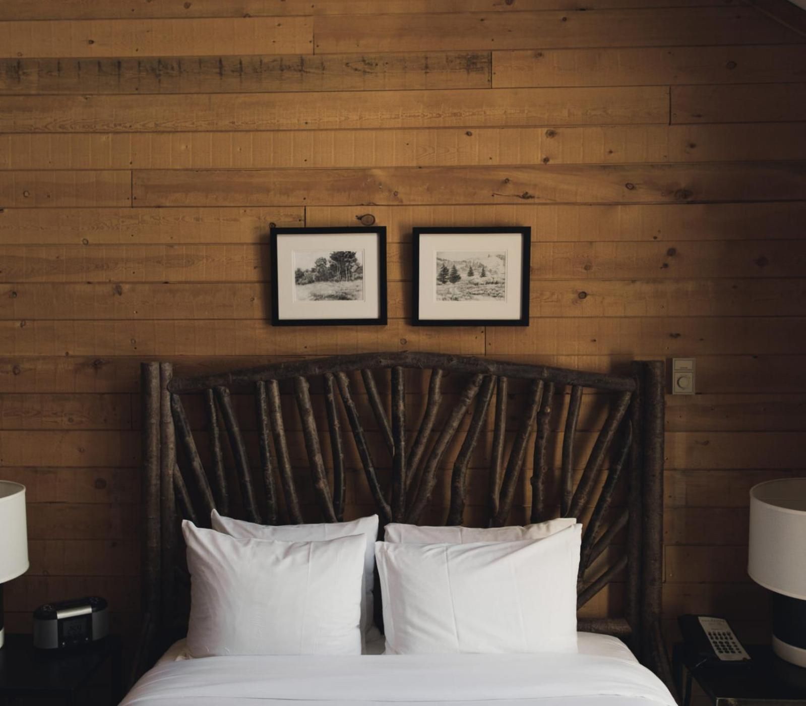 Rustic branch headboards and warm wood paneling create an intimate mountain sanctuary, where black-and-white landscape prints echo the wilderness beyond your window.