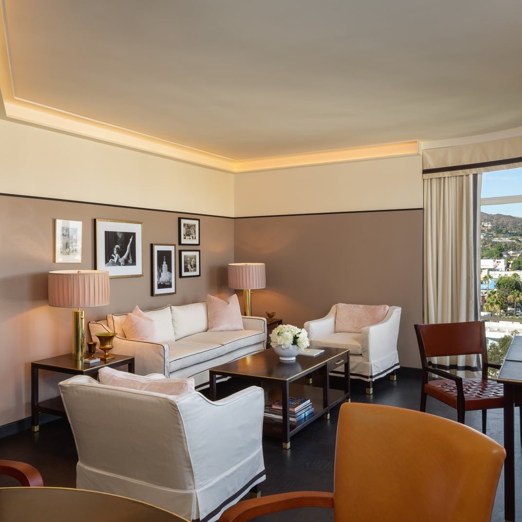 Warm brass lamps and blush tones create an intimate living space where floor-to-ceiling windows frame sweeping views of the Hollywood Hills below.