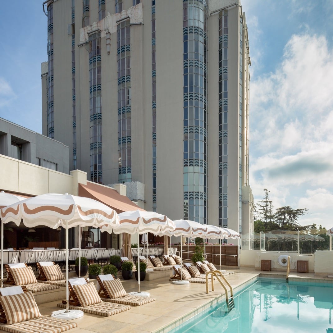 Striped lounge chairs and scalloped umbrellas create a chic poolside retreat high above the city, where Art Deco glamour meets contemporary California cool.