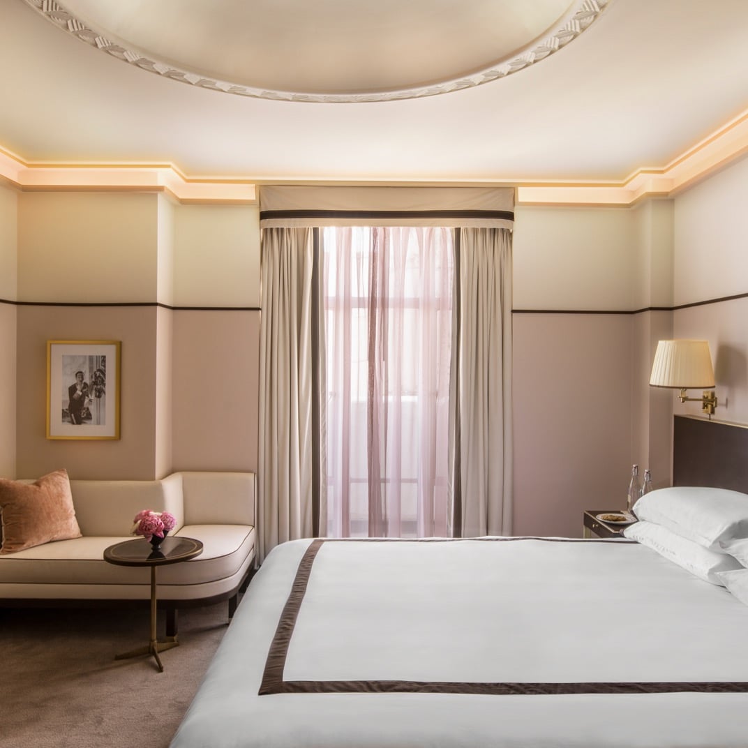 Blush-toned walls and curved crown molding create intimate elegance in this thoughtfully appointed guest room, where warm lighting casts a golden glow across plush linens and vintage-inspired furnishings.