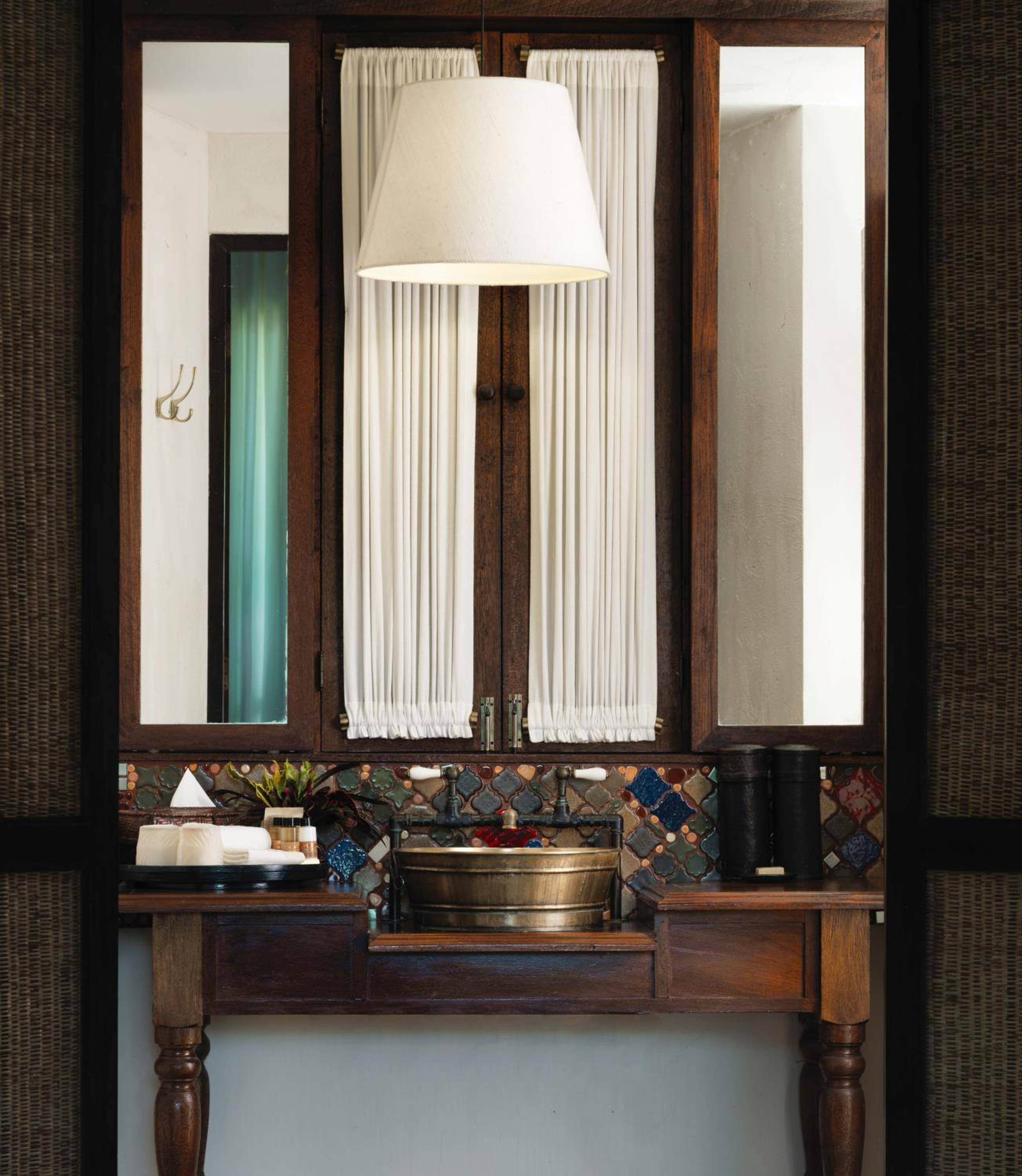 Handcrafted mosaic tiles frame a brass basin atop rich teak vanity, where traditional Lanna design meets modern luxury in thoughtfully appointed guest bathrooms.