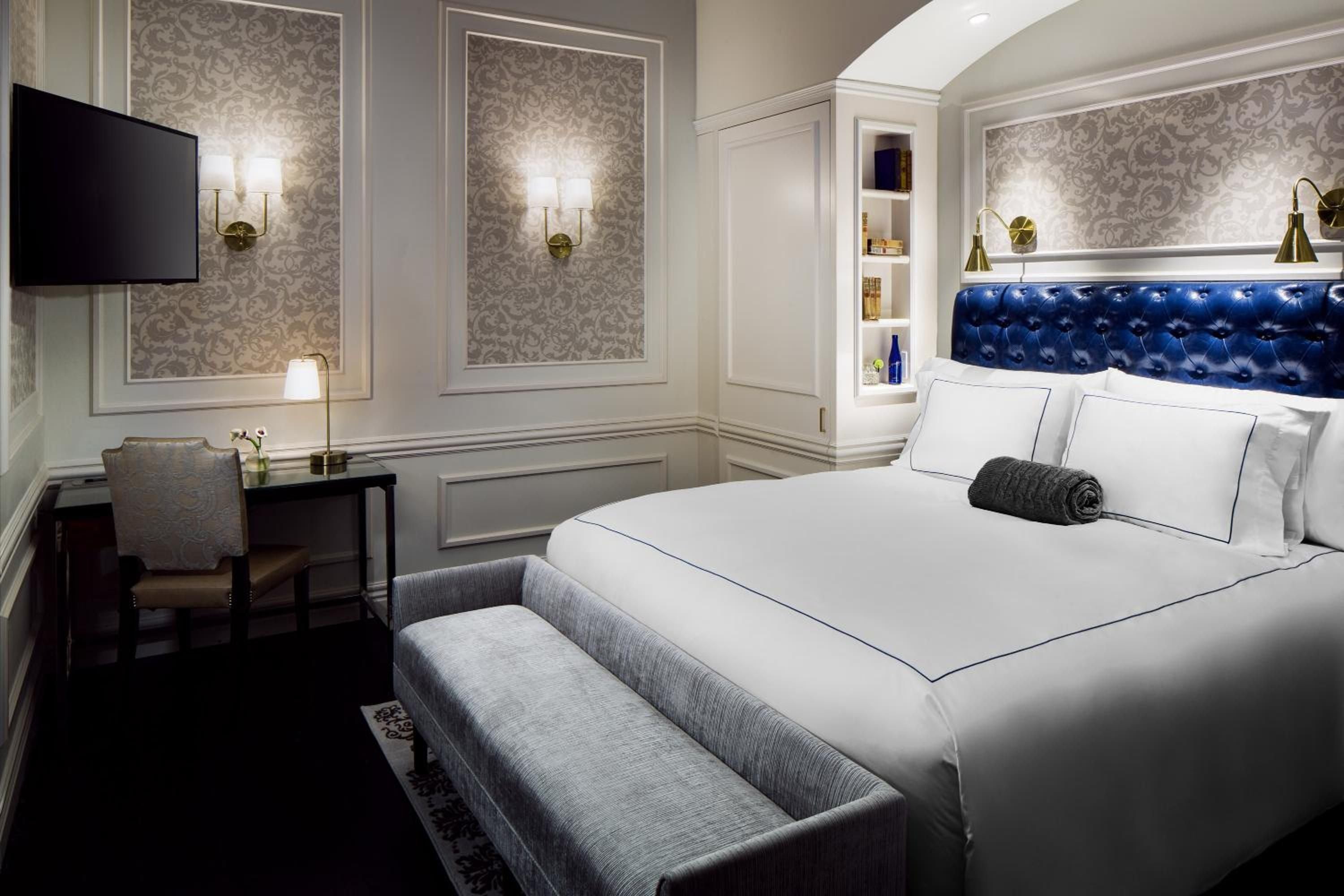 Sophisticated quarters blend classic elegance with modern comfort, featuring rich blue tufted headboards, damask wallpaper, and brass sconces that cast intimate pools of light.