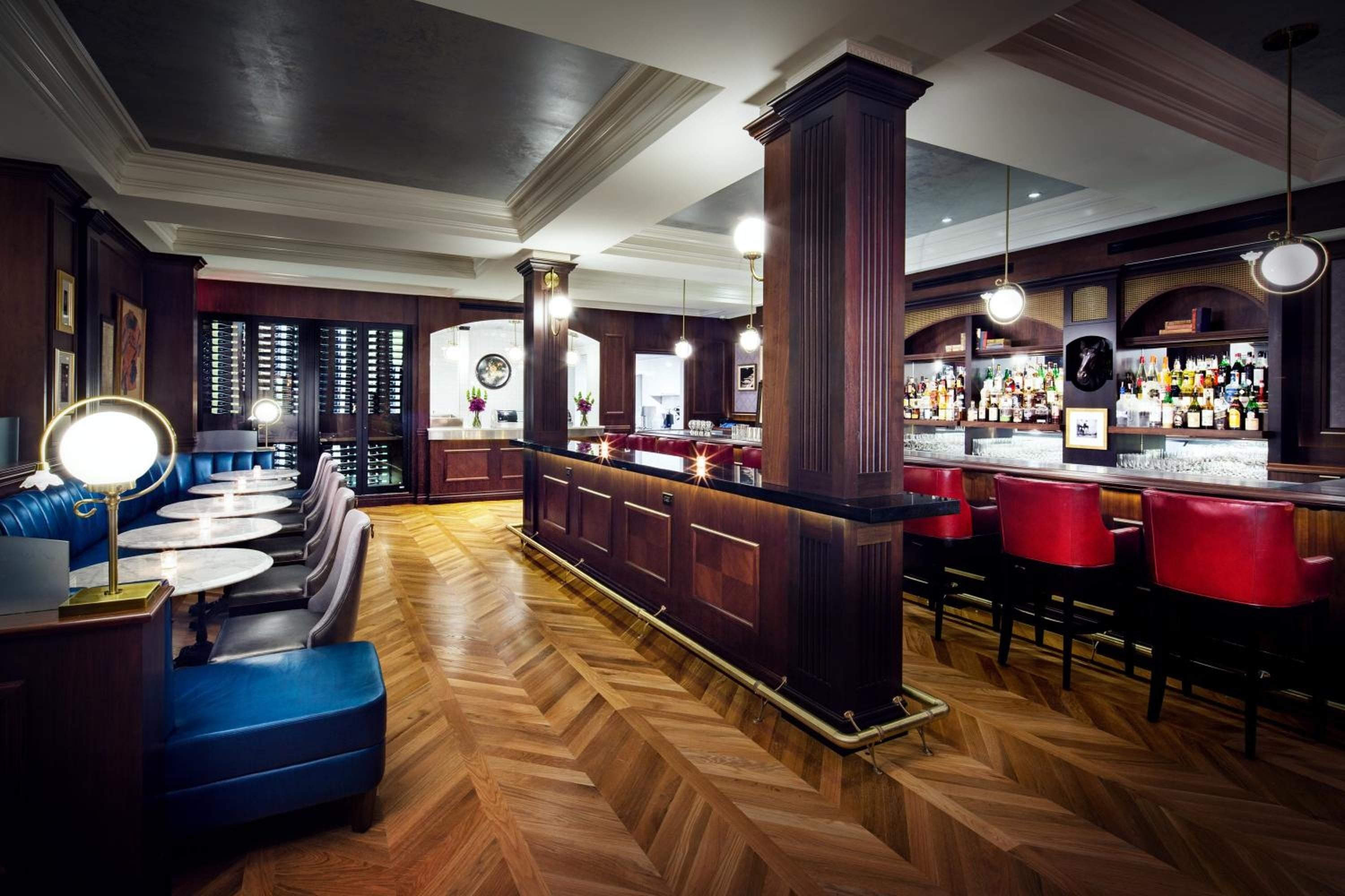 Rich mahogany paneling and herringbone parquet floors create an intimate setting where crimson leather stools invite lingering over craft cocktails beneath coffered ceilings.